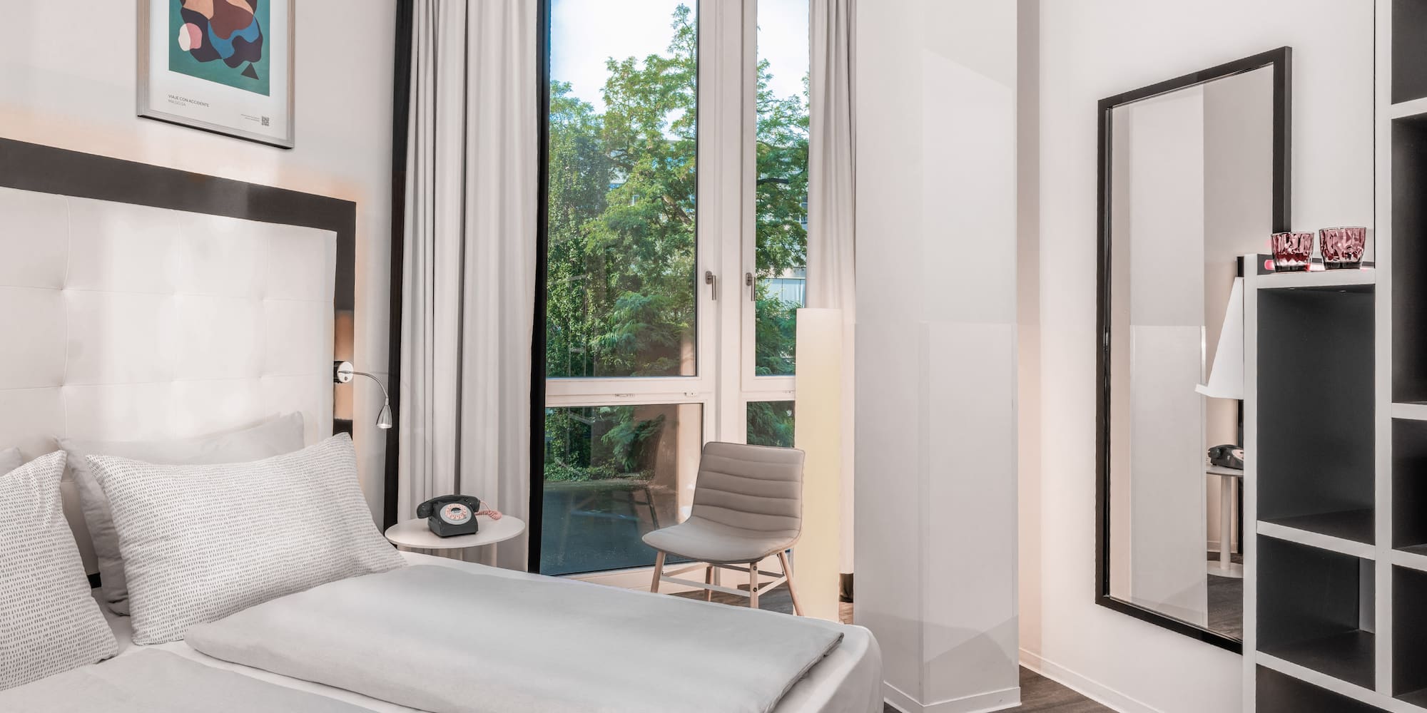 Modern hotel room, white bed, window with green trees view.