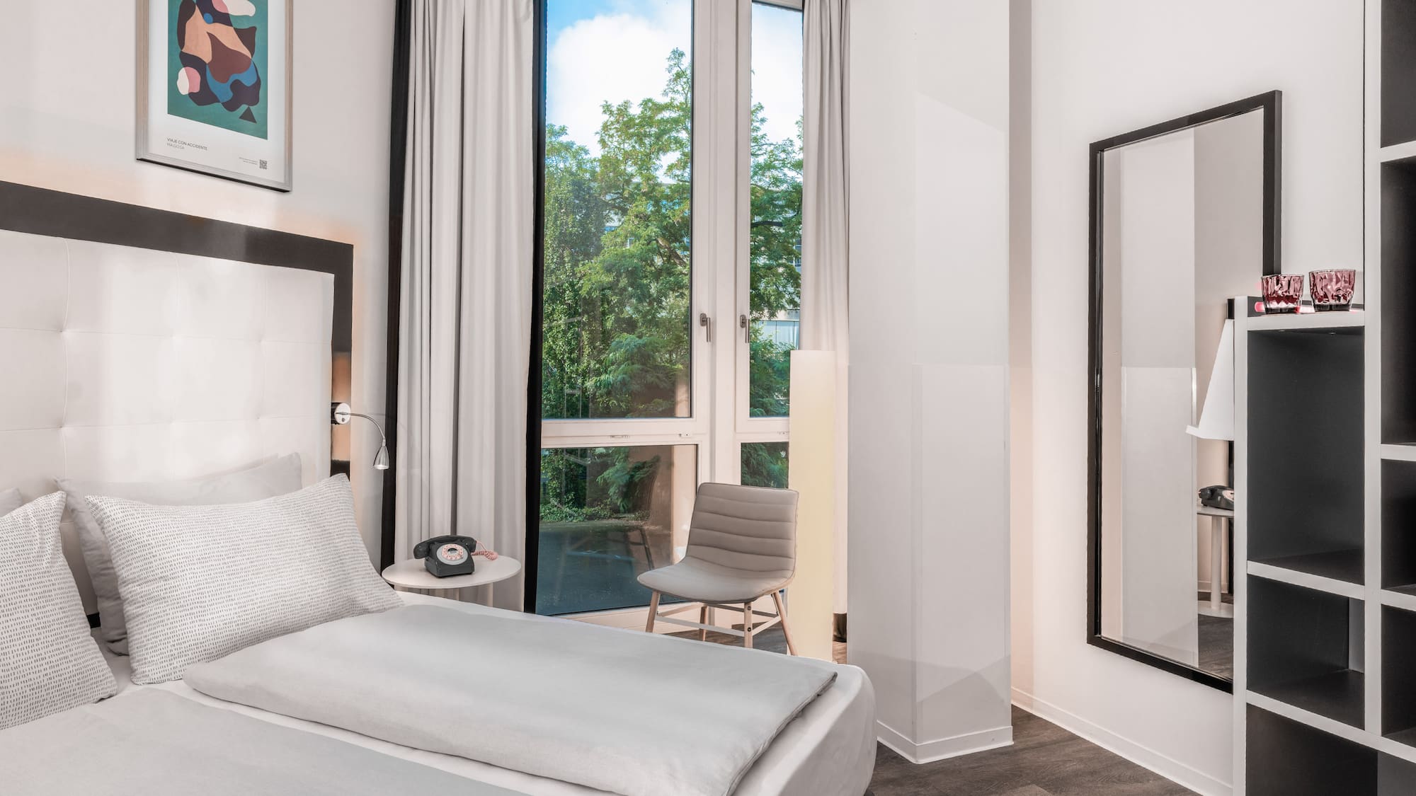 Modern hotel room, white bed, window with green trees view.