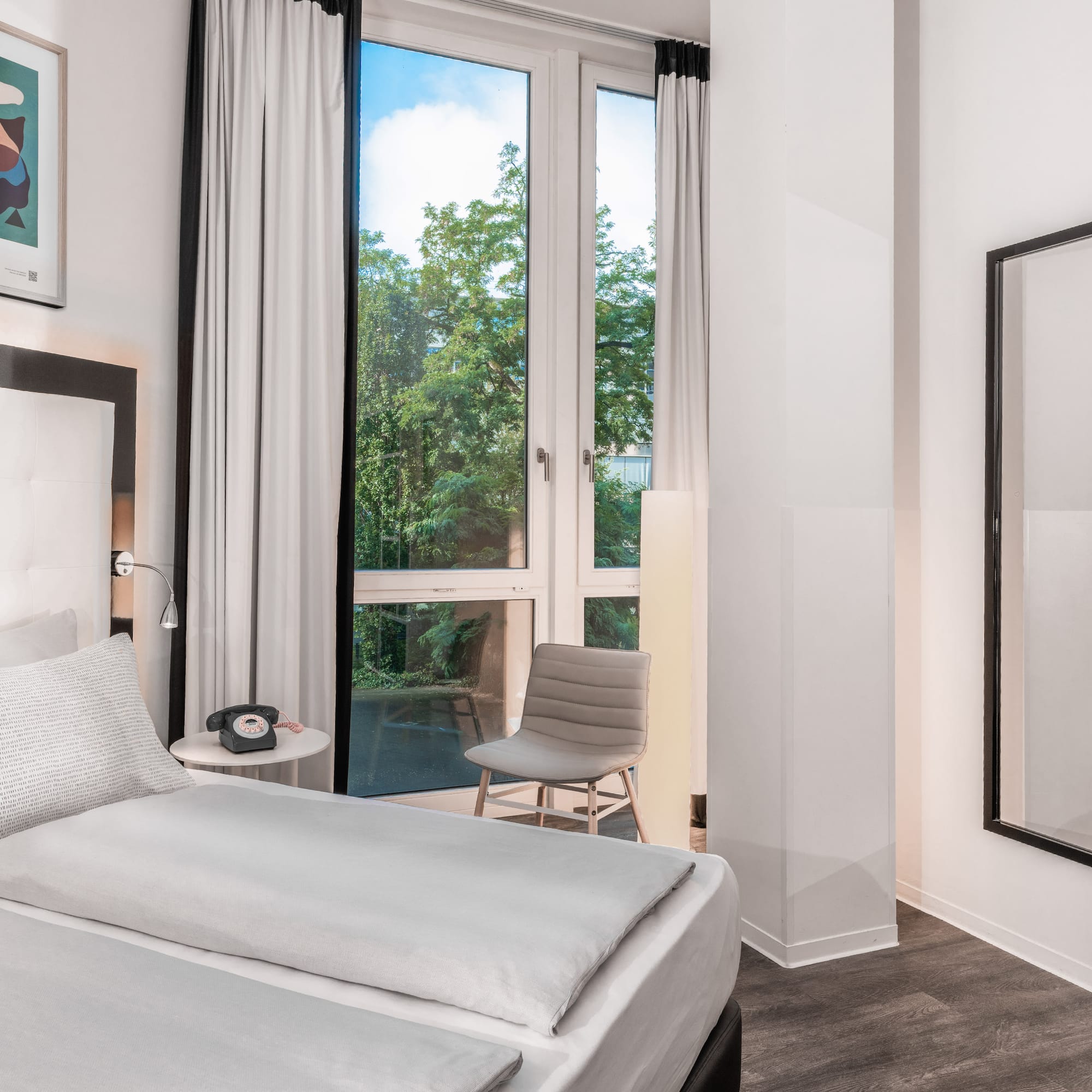 Modern hotel room, white bed, window with green trees view.
