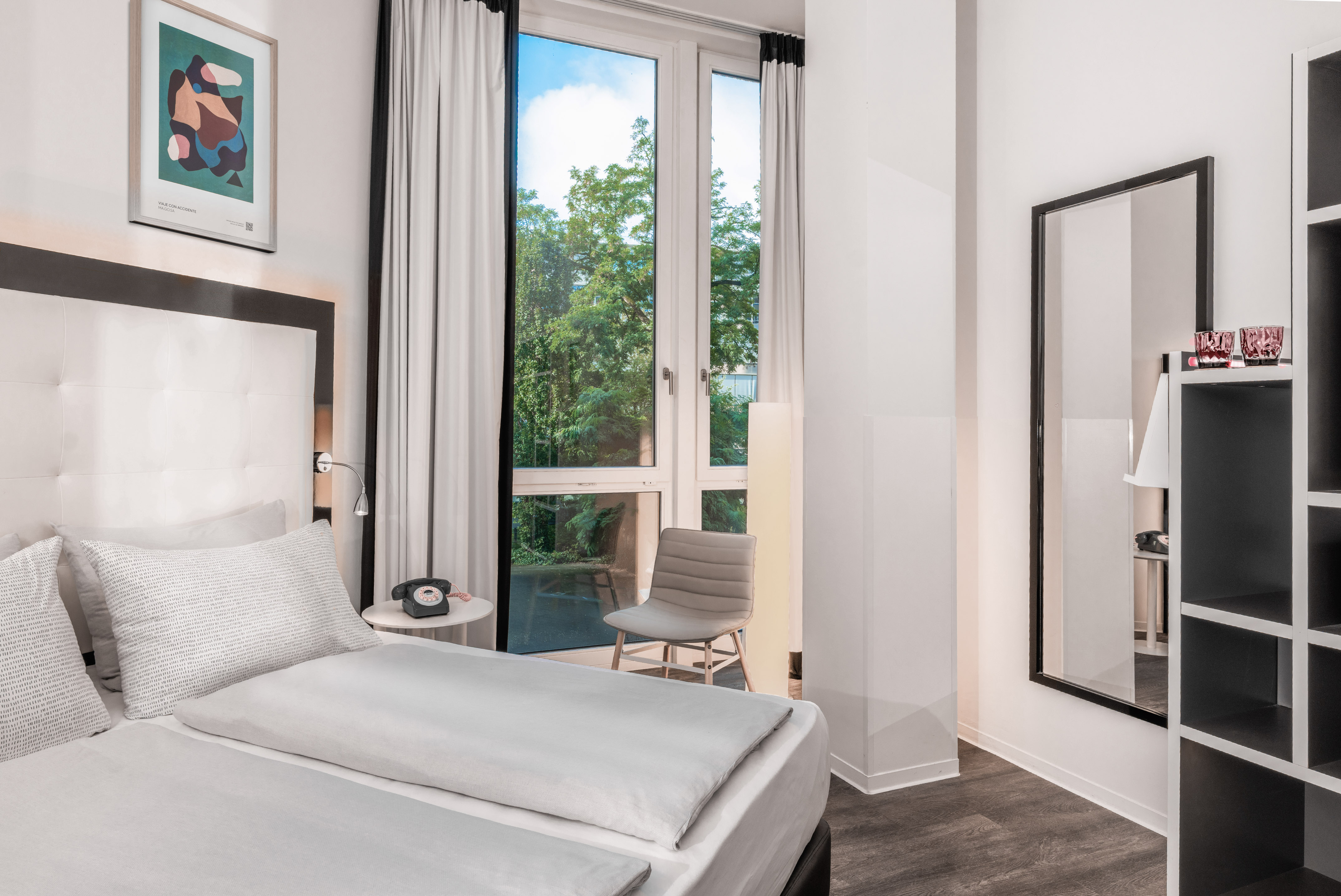 Modern hotel room, white bed, window with green trees view.