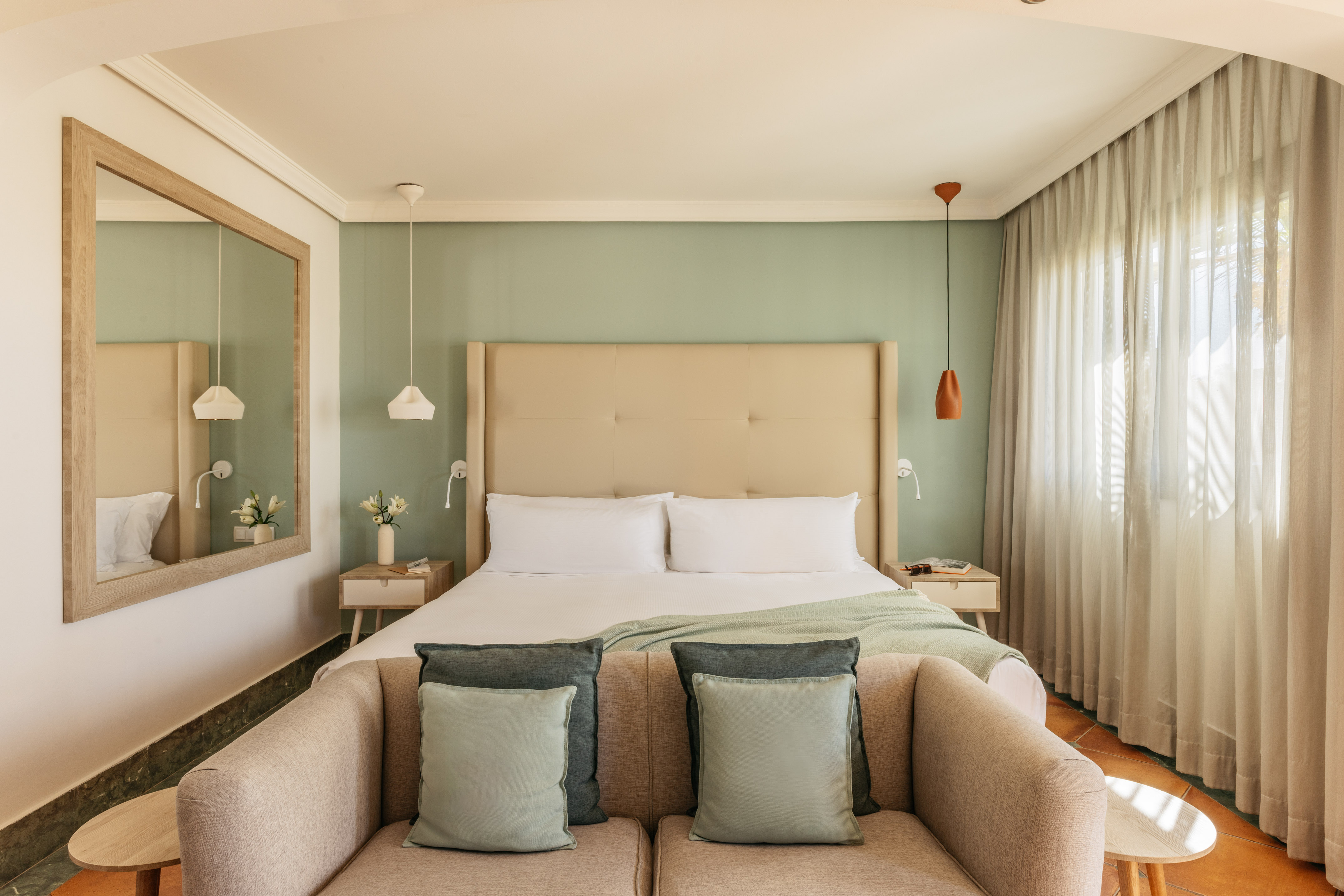 Cozy modern hotel bedroom featuring a green wall, large bed, and comfortable sofa.