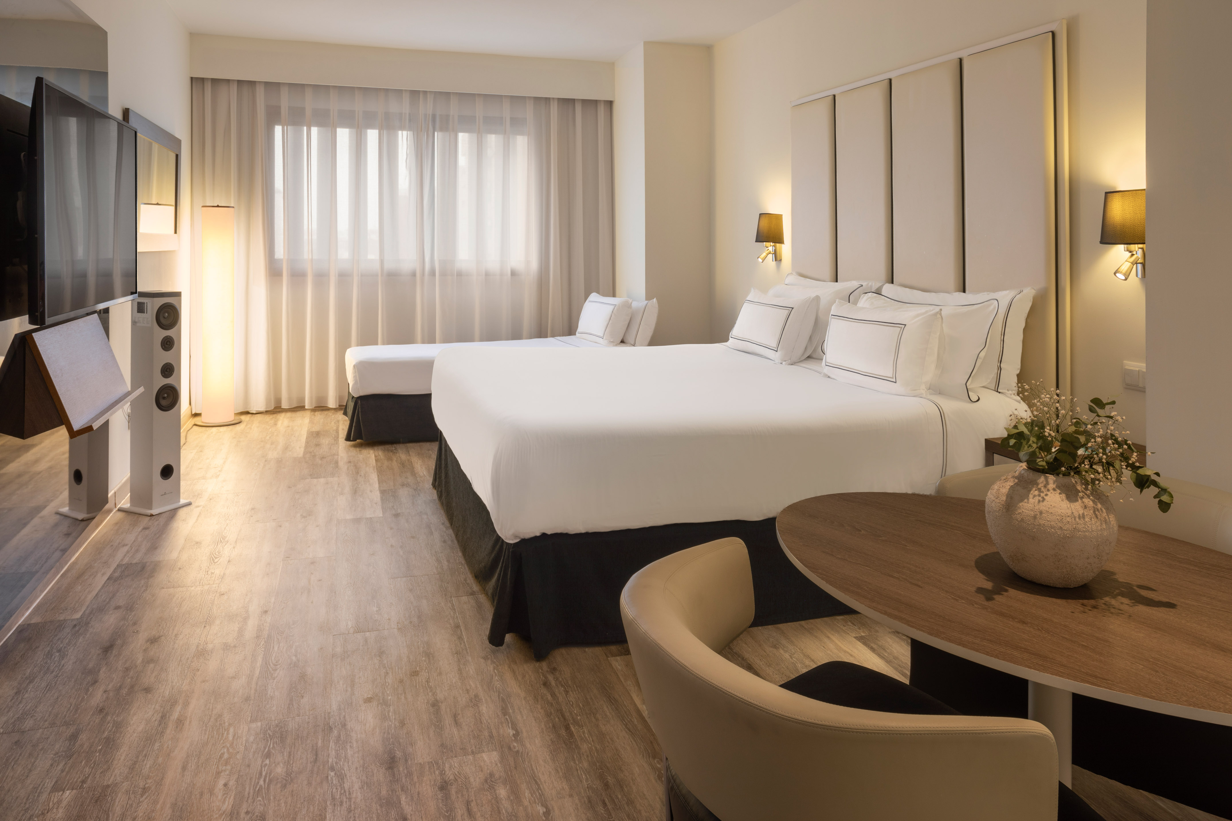 Spacious hotel room with two beds, wood floor, TV, and seating area.