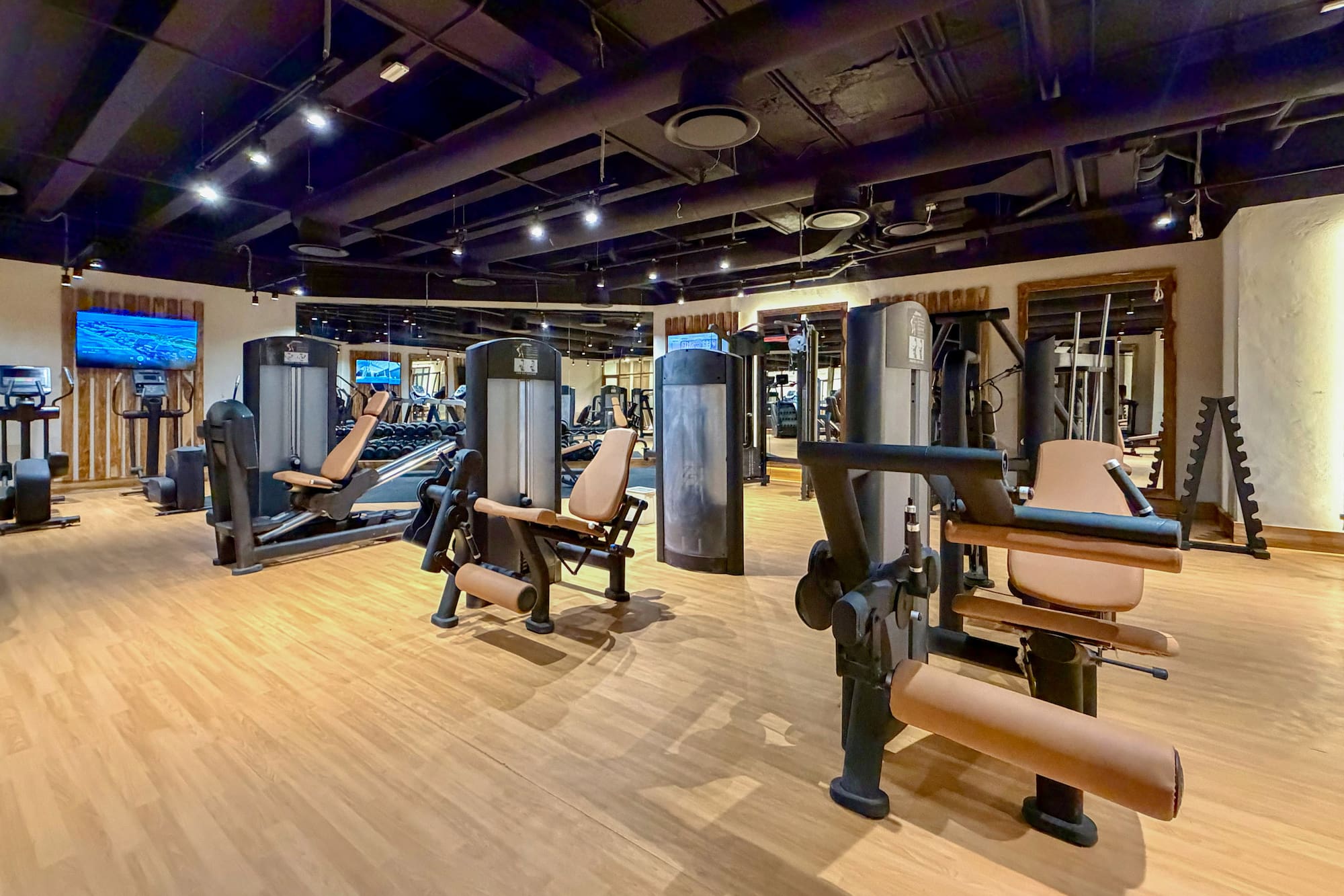 Hotel gym with weight machines, cardio equipment, and light hardwood floor.