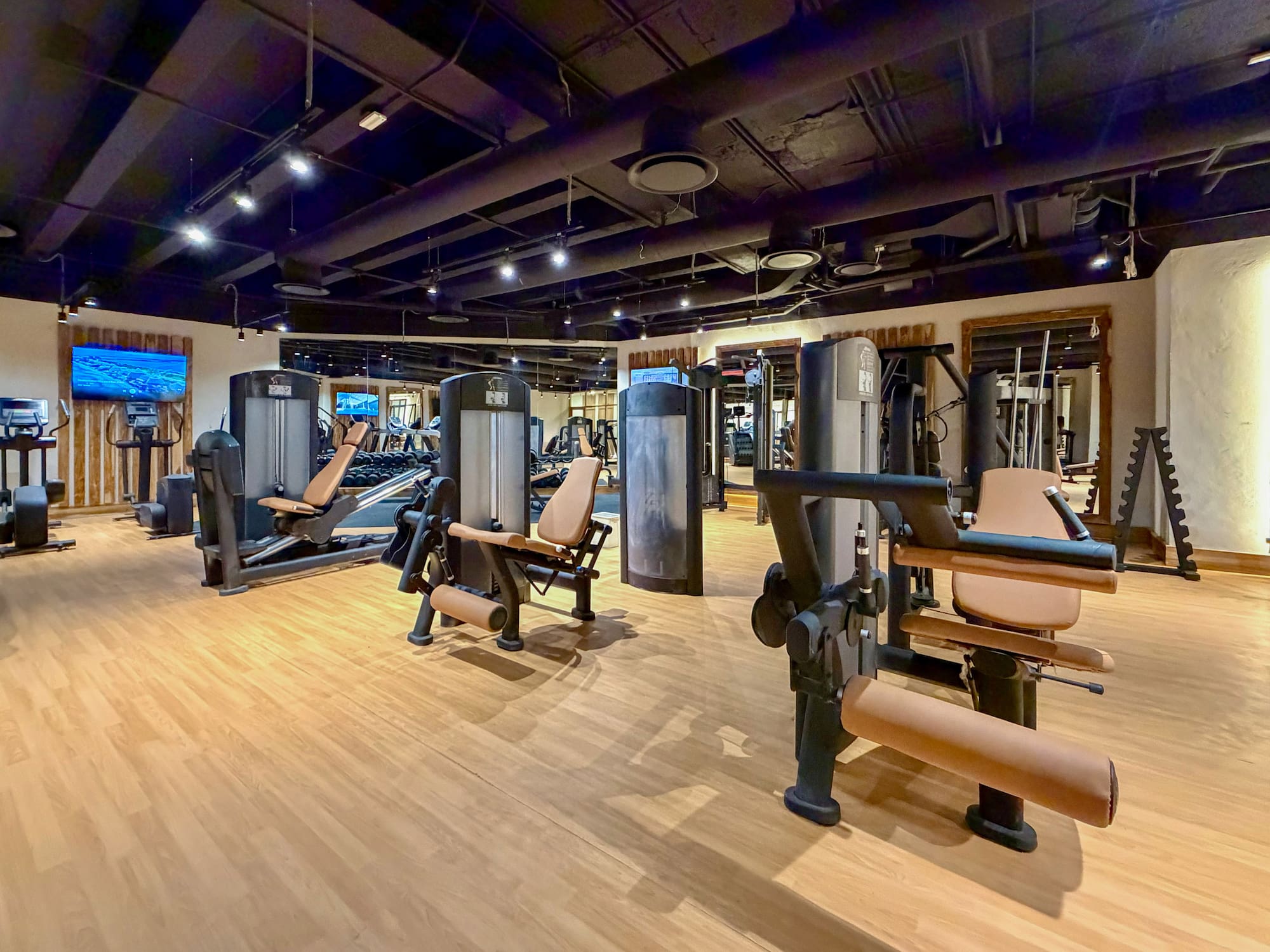 Hotel gym with weight machines, cardio equipment, and light hardwood floor.