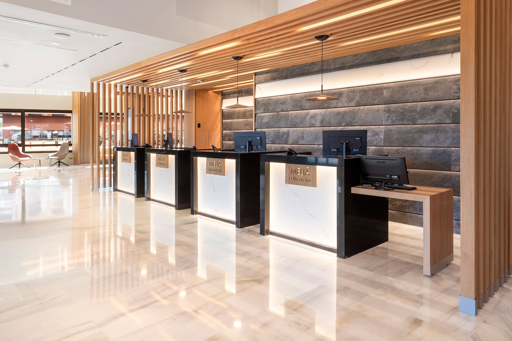 Melia Costa del Sol hotel reception with modern desks, marble floor, wood slats.