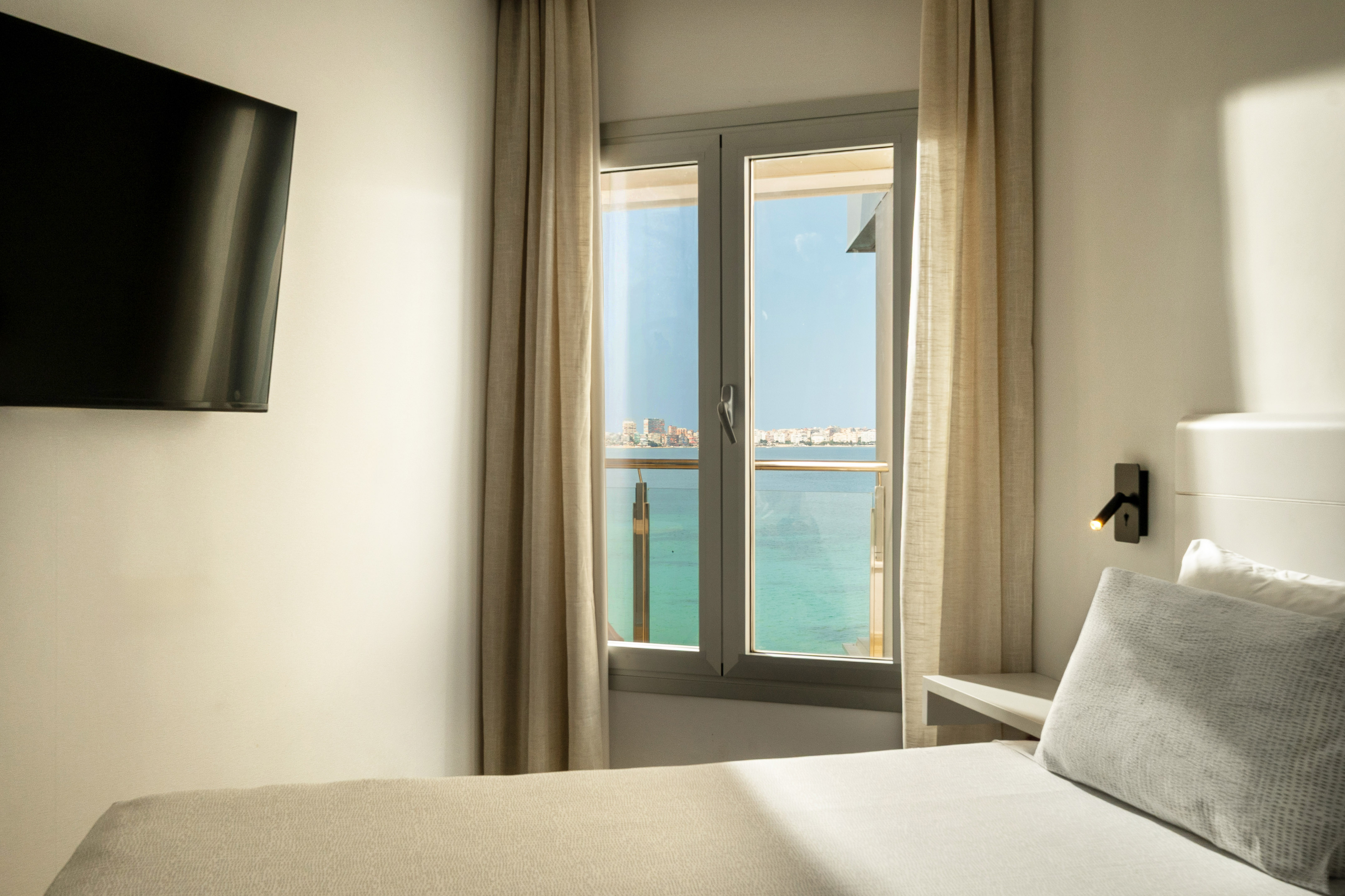 Hotel room with ocean view window, bed, and wall-mounted television.