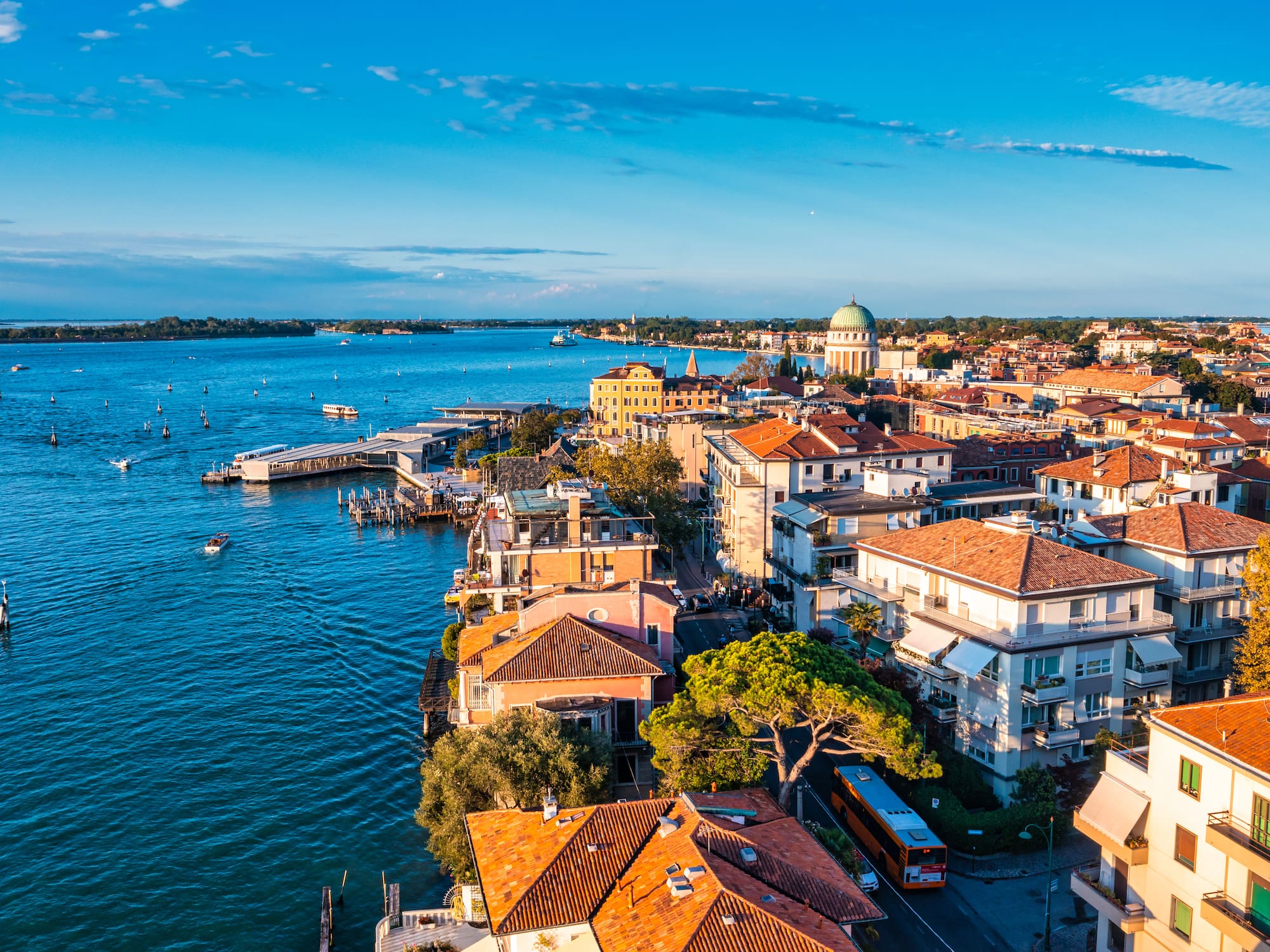 Lido di Venezia cityscape: red-roofed buildings, historic dome, blue lagoon.