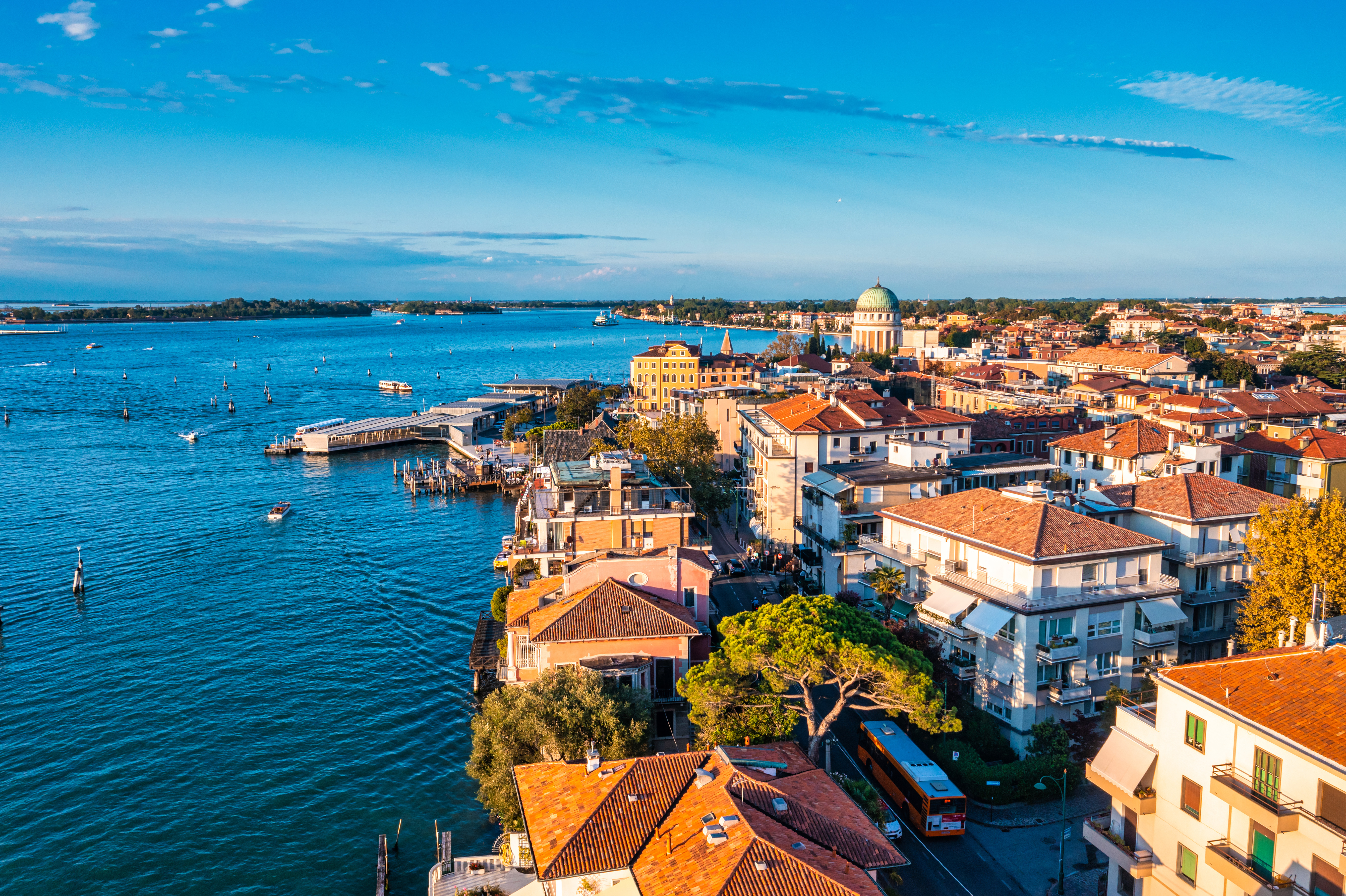 Lido di Venezia cityscape: red-roofed buildings, historic dome, blue lagoon.