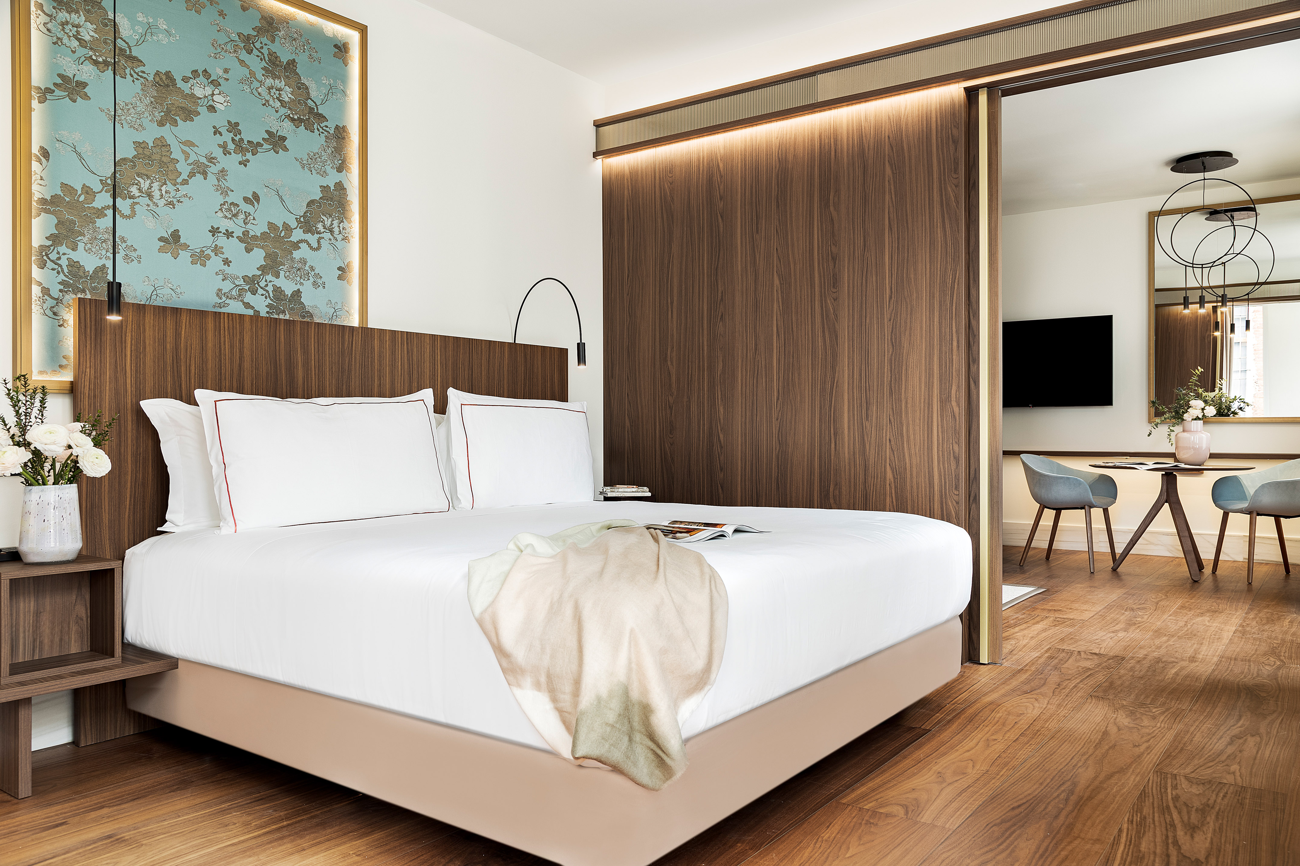 Luxury hotel bedroom with wood paneling, floral wall art, and separate lounge.