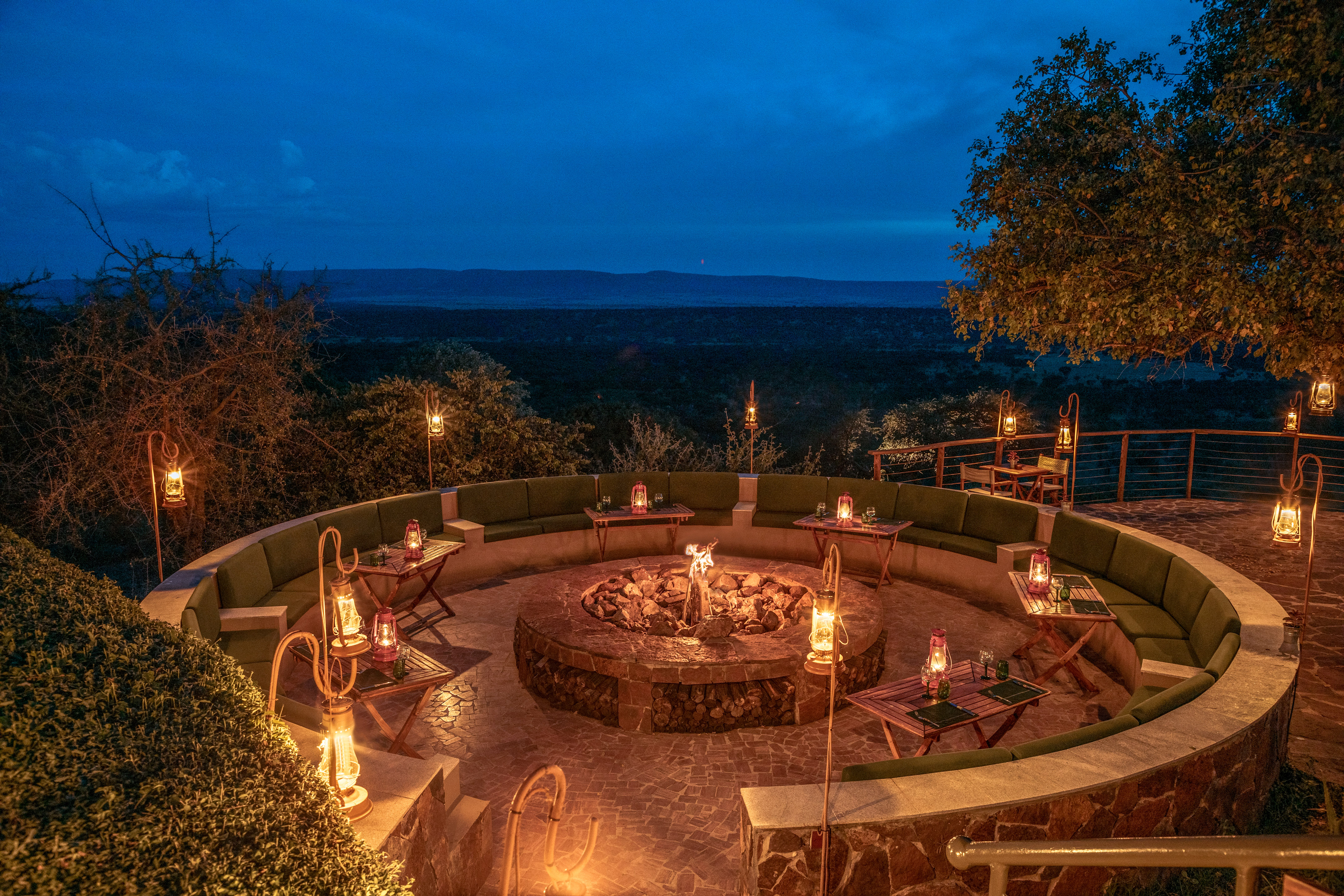 Safari lodge fire pit lounge, dusk, lanterns, and scenic mountain views.