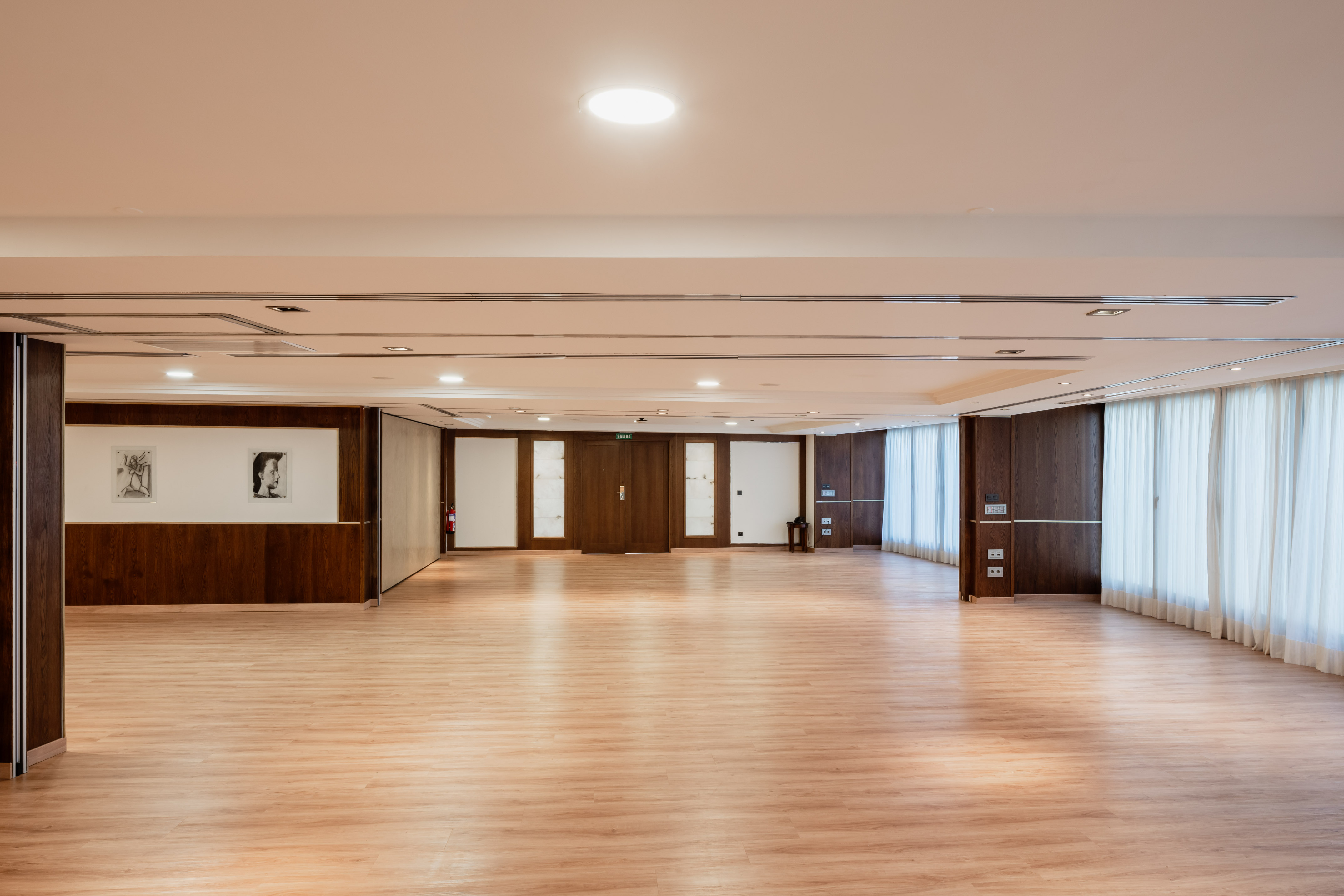 Empty modern event space with wood floor, dark panels, and white curtains.
