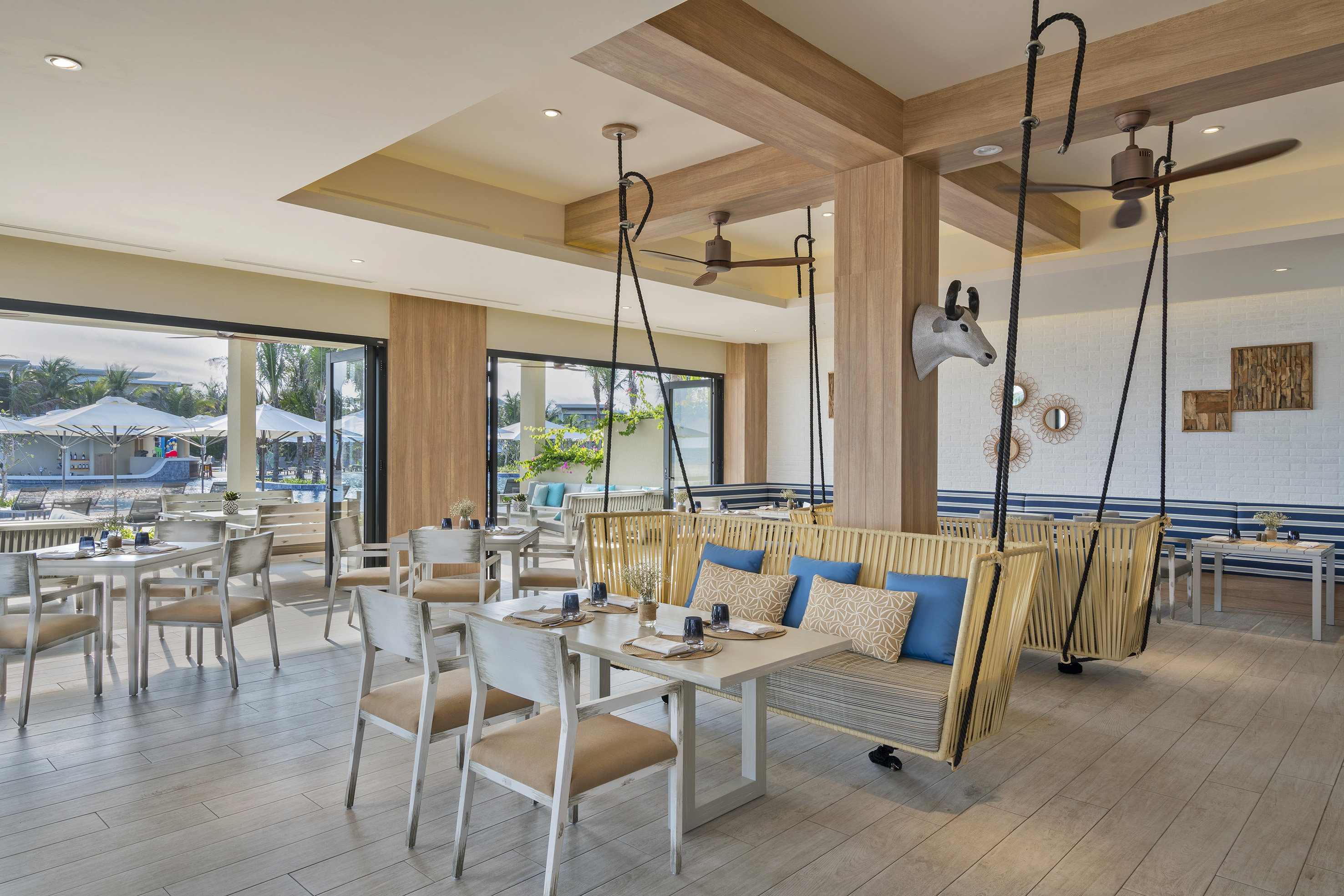 Modern resort restaurant with unique swing seating, light wood decor, and pool view.