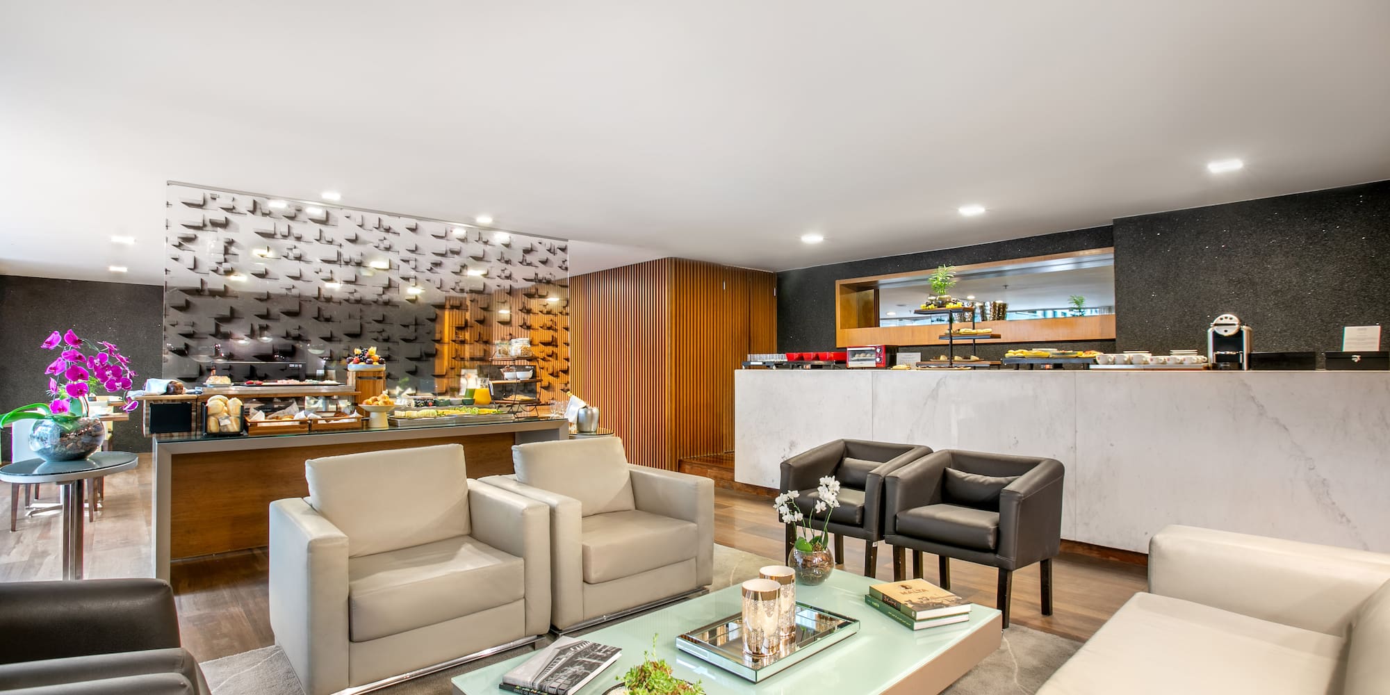 Hotel lounge with modern seating, breakfast buffet, and coffee station.