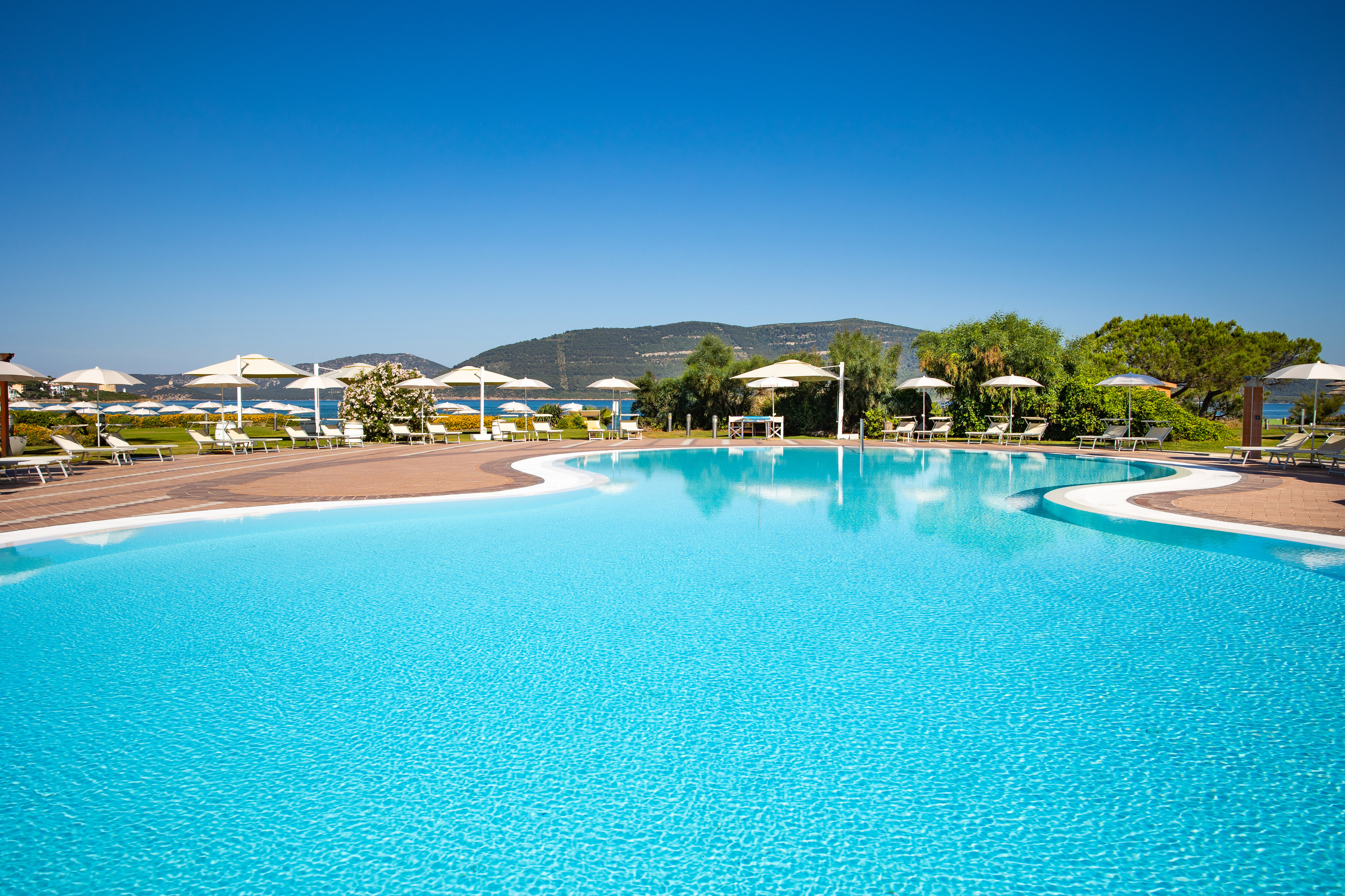 Mediterranean resort pool with sunbeds, umbrellas, and ocean views.