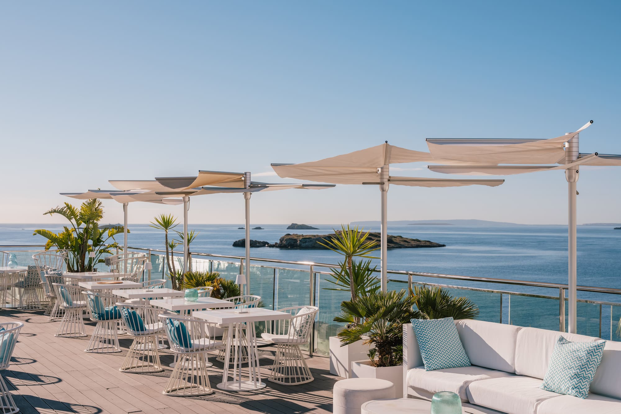 Rooftop terrace with sea view, white dining and lounge furniture, sun shades.