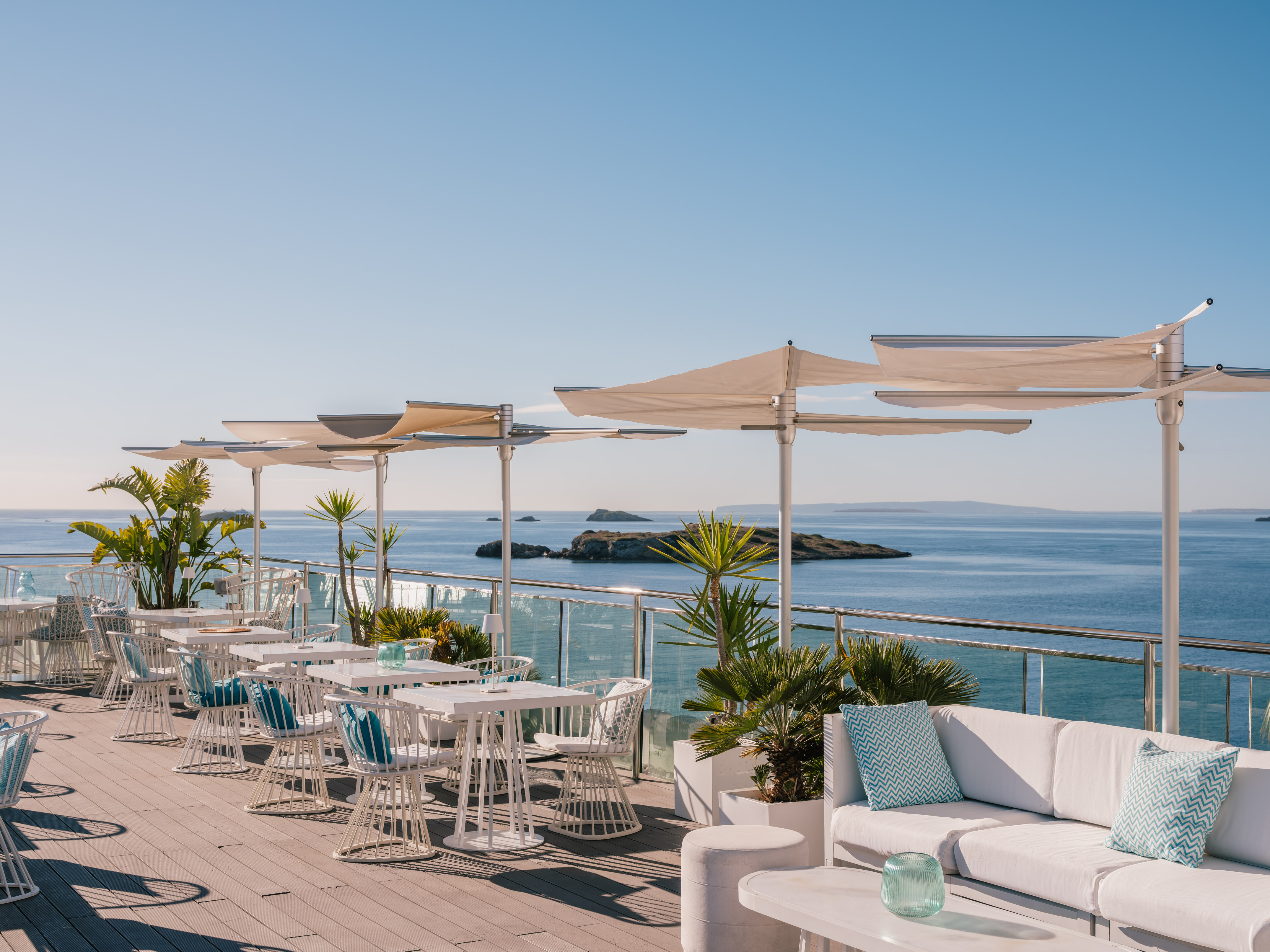 Rooftop terrace with sea view, white dining and lounge furniture, sun shades.