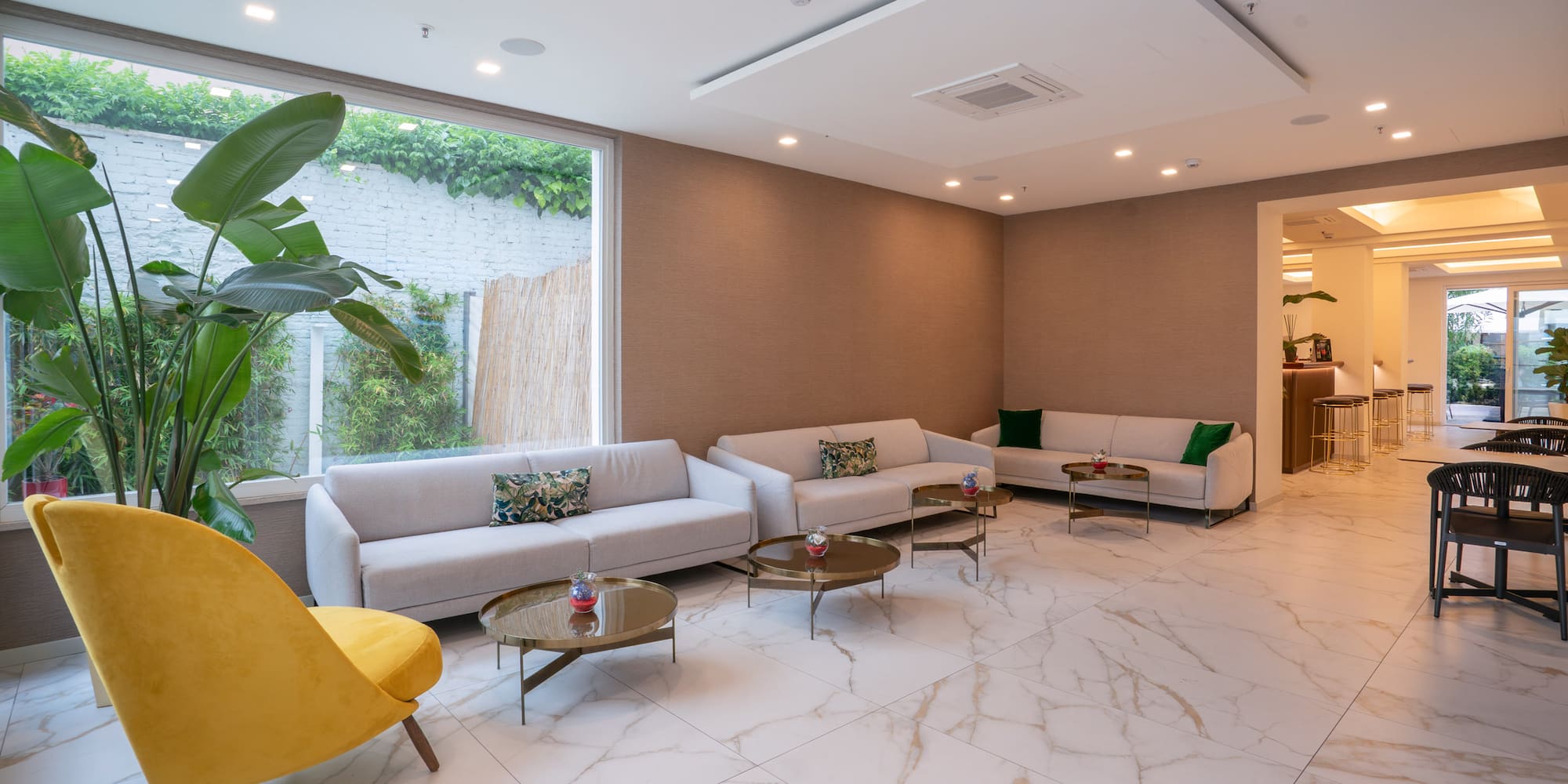 Modern hotel lounge with white sofas, yellow chair, gold tables, marble floor.