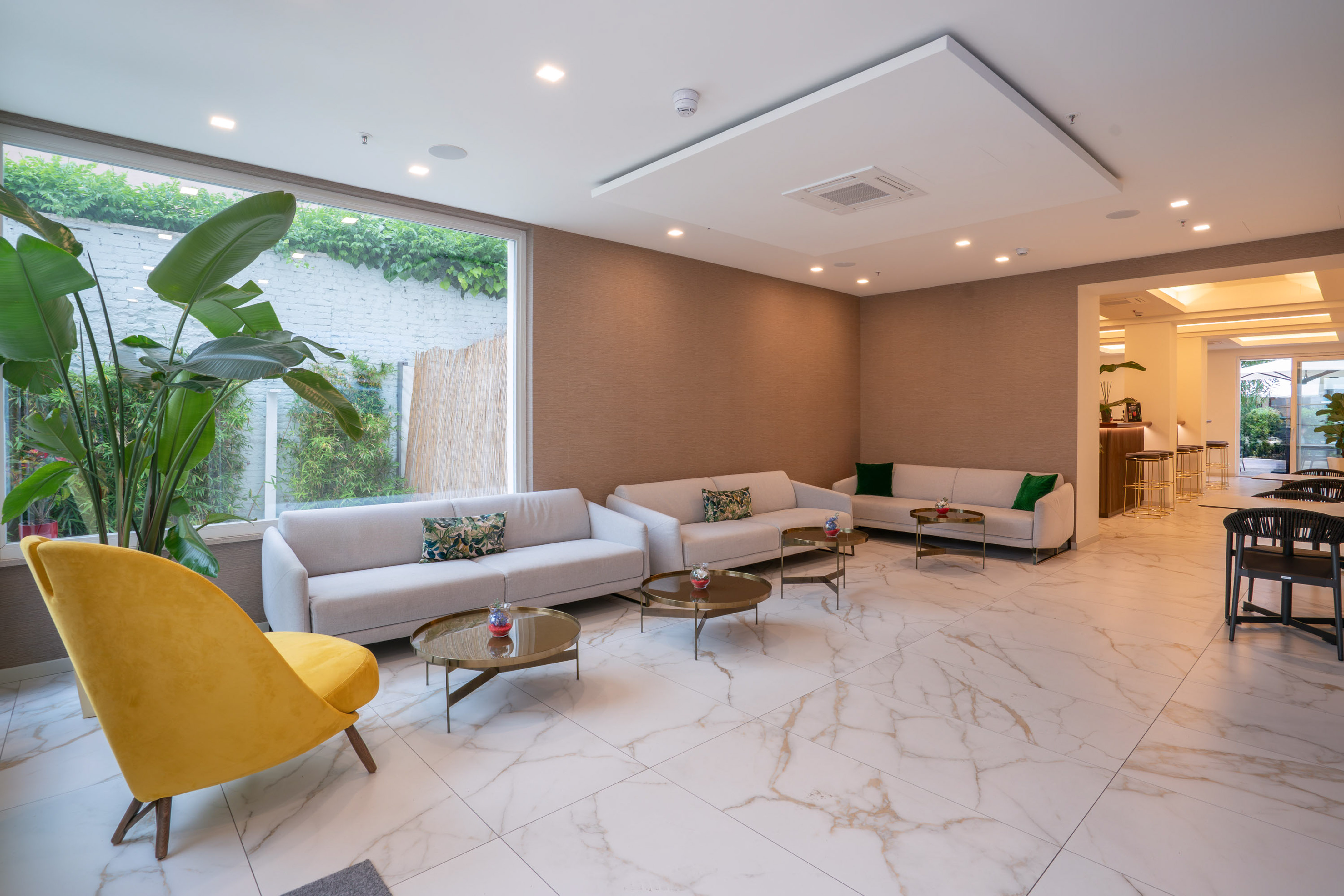 Modern hotel lounge with white sofas, yellow chair, gold tables, marble floor.