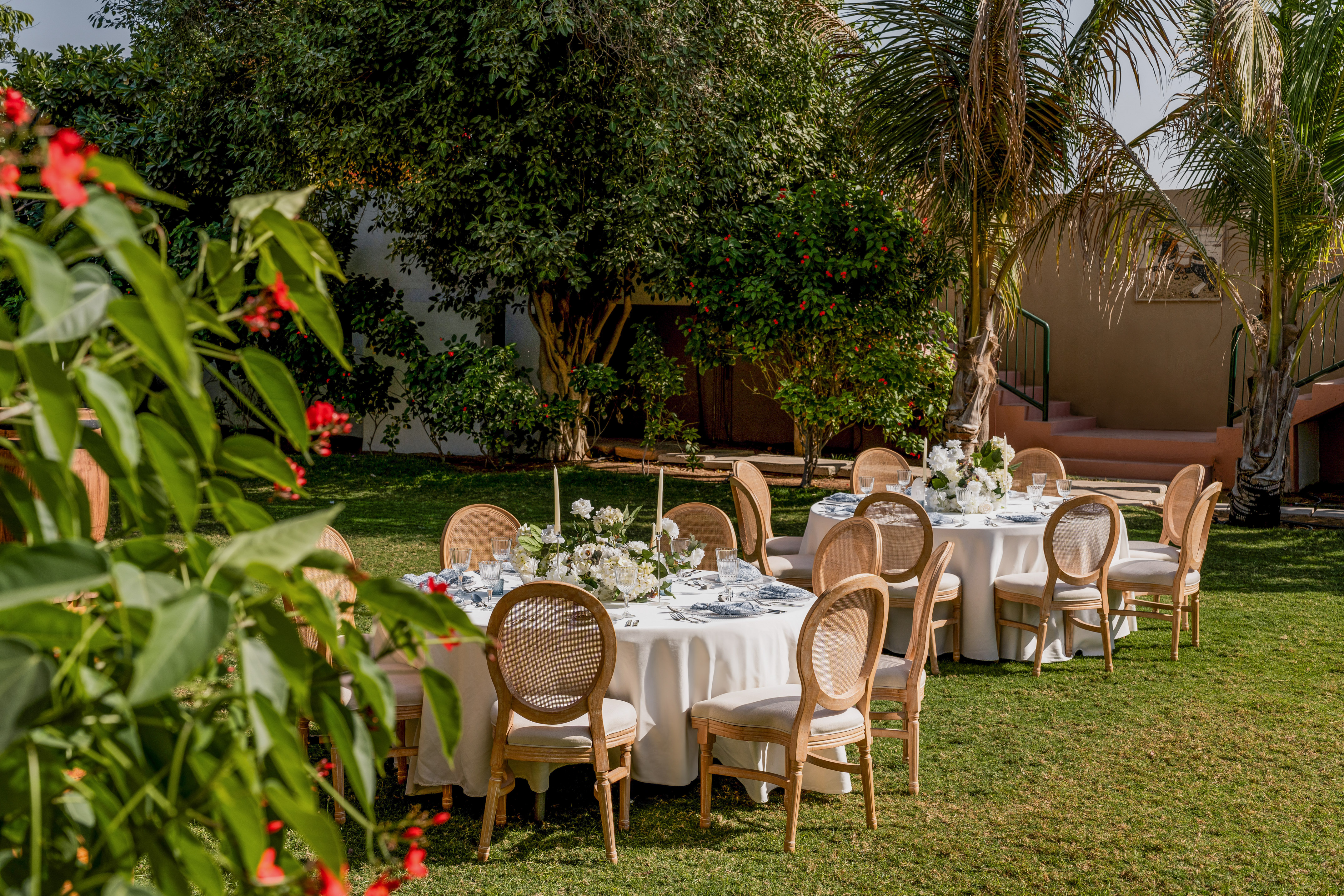 Outdoor garden dining setup with elegant tables, white linens, wicker chairs.