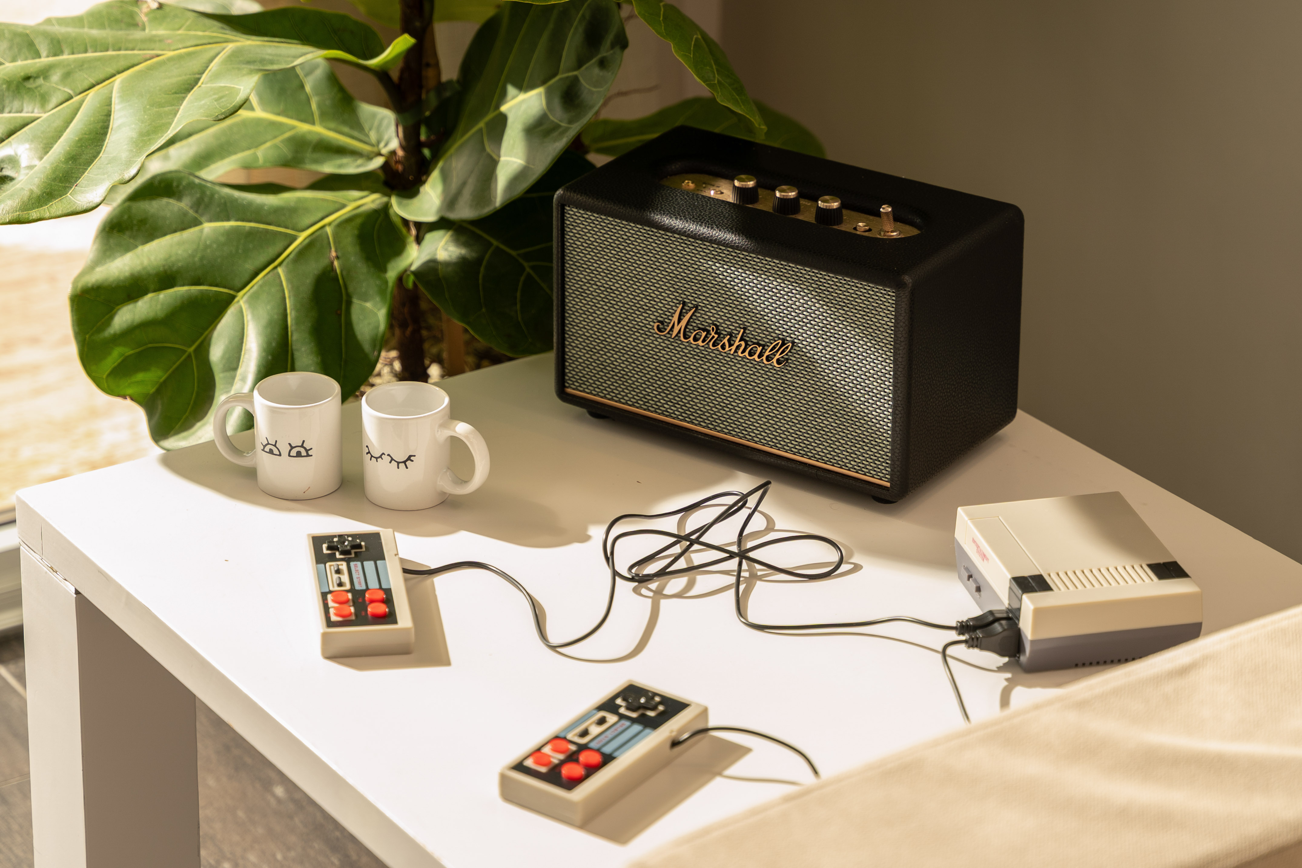 Retro gaming setup with NES console, controllers, Marshall speaker, and mugs.