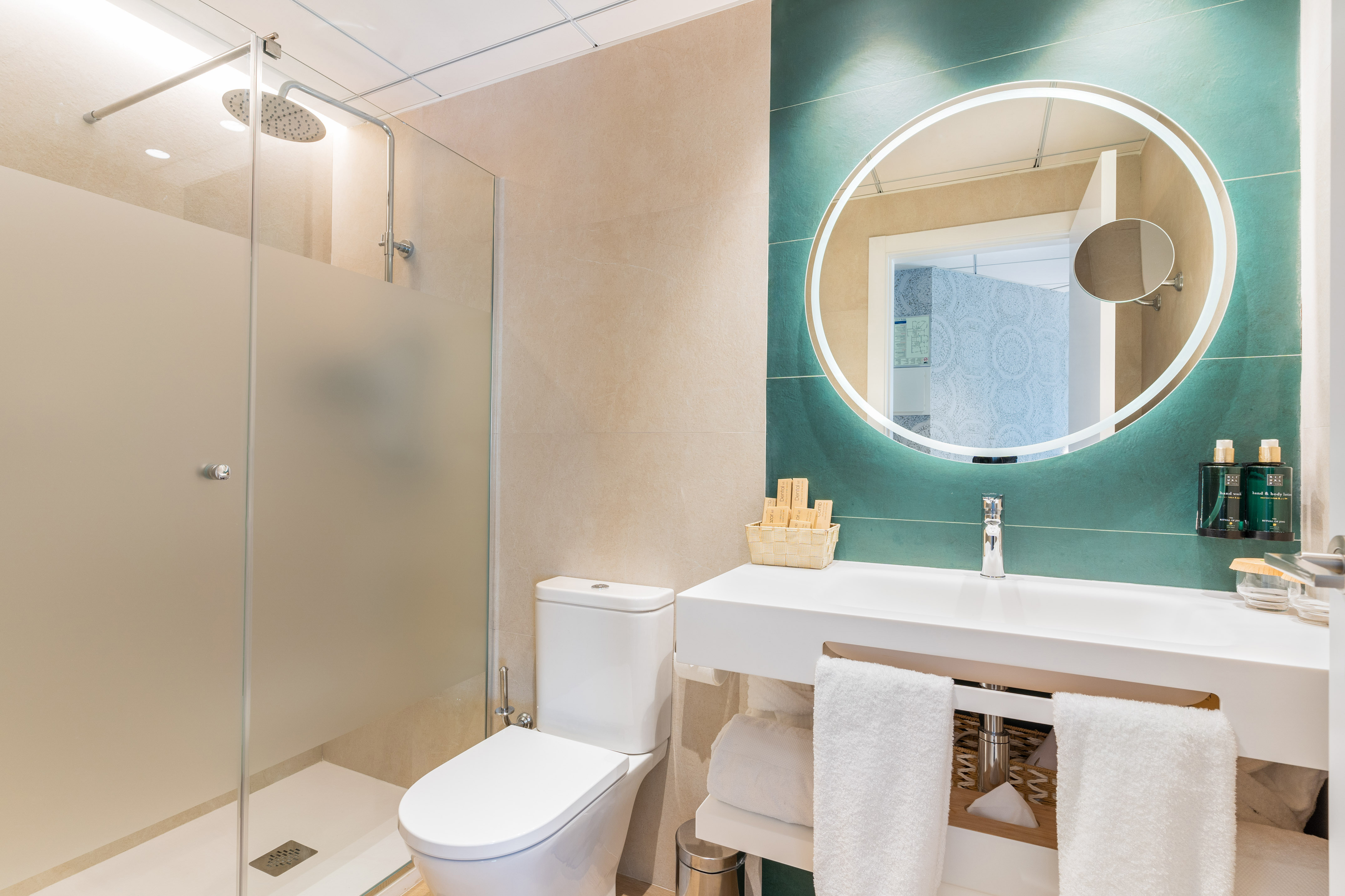 Modern bathroom with walk-in shower, toilet, vanity, and backlit round mirror.