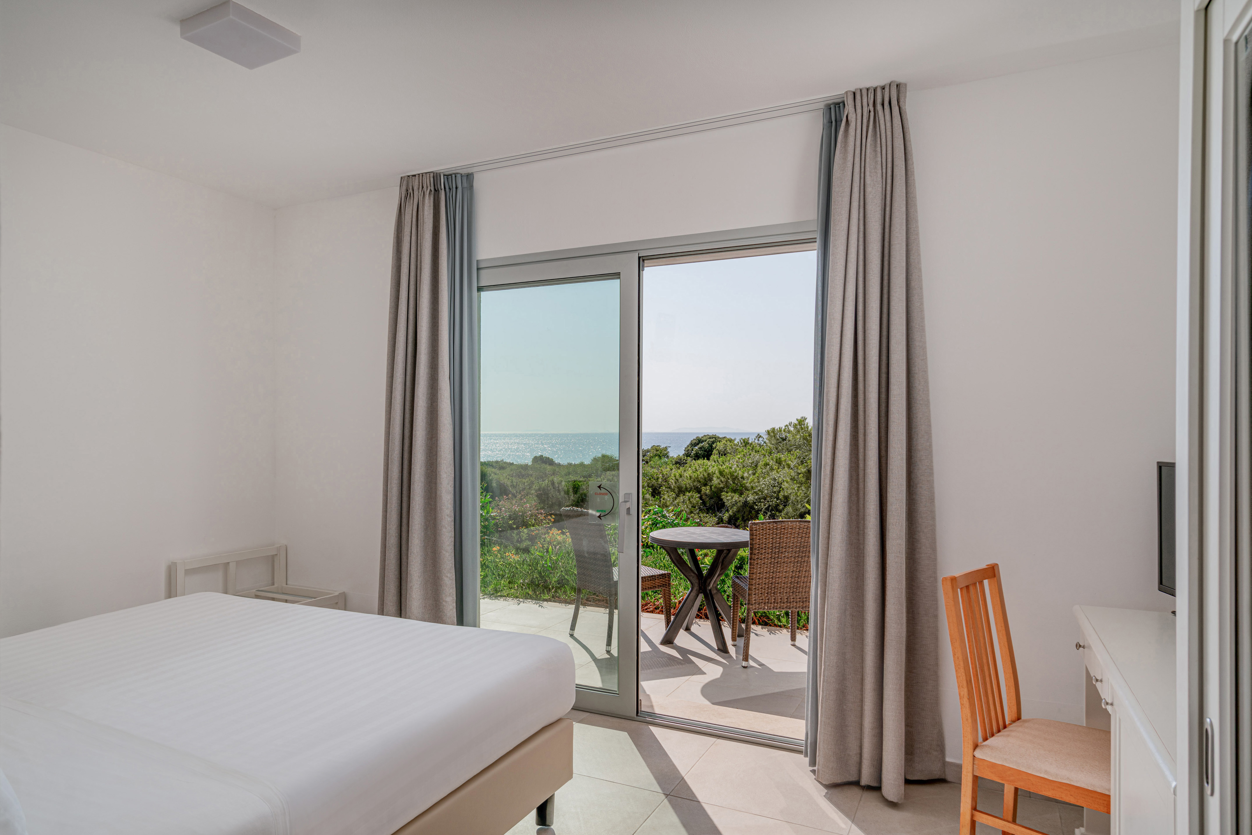 Hotel bedroom with sea view balcony and outdoor seating.