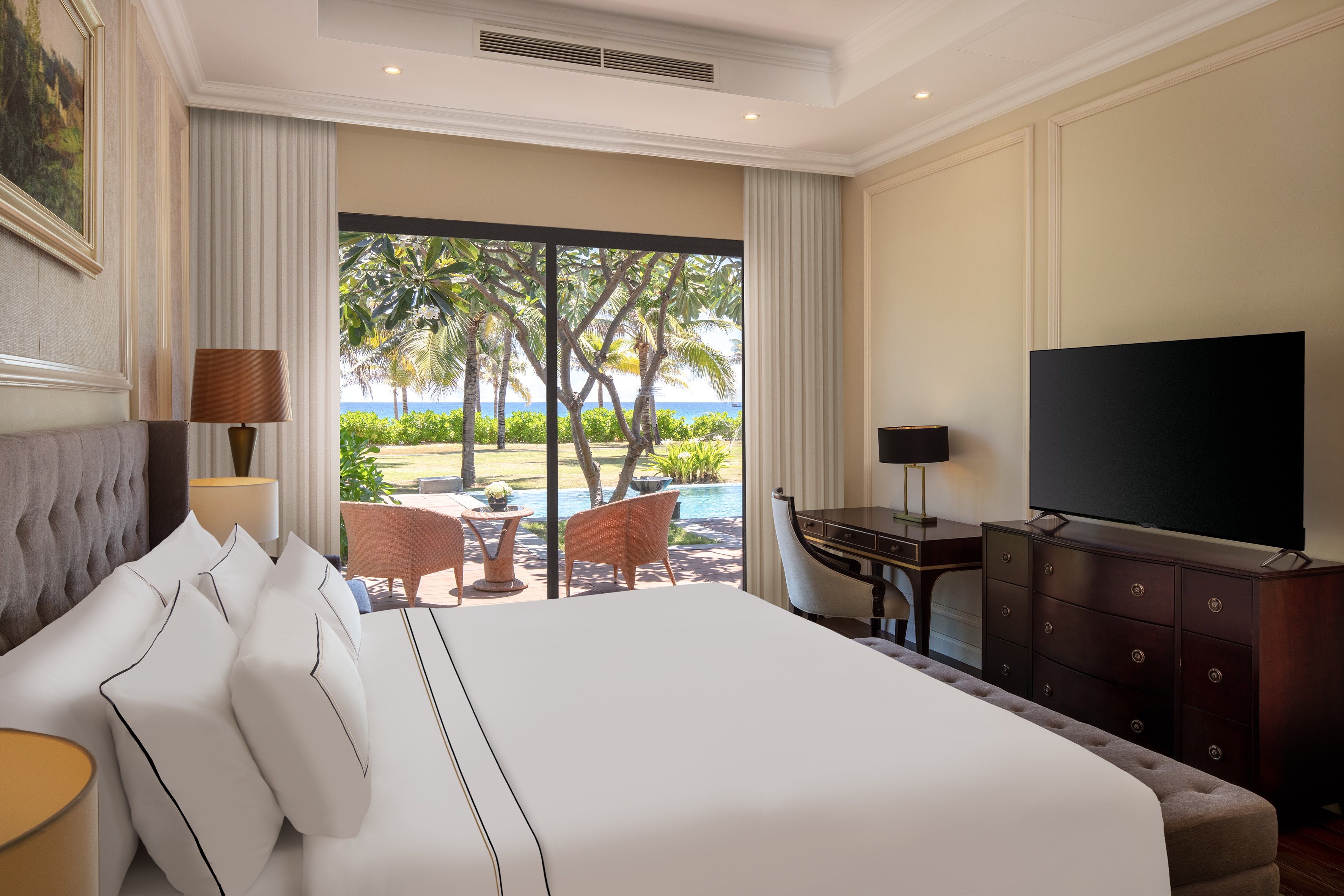 Elegant hotel bedroom with king bed, ocean view, and tropical garden patio.