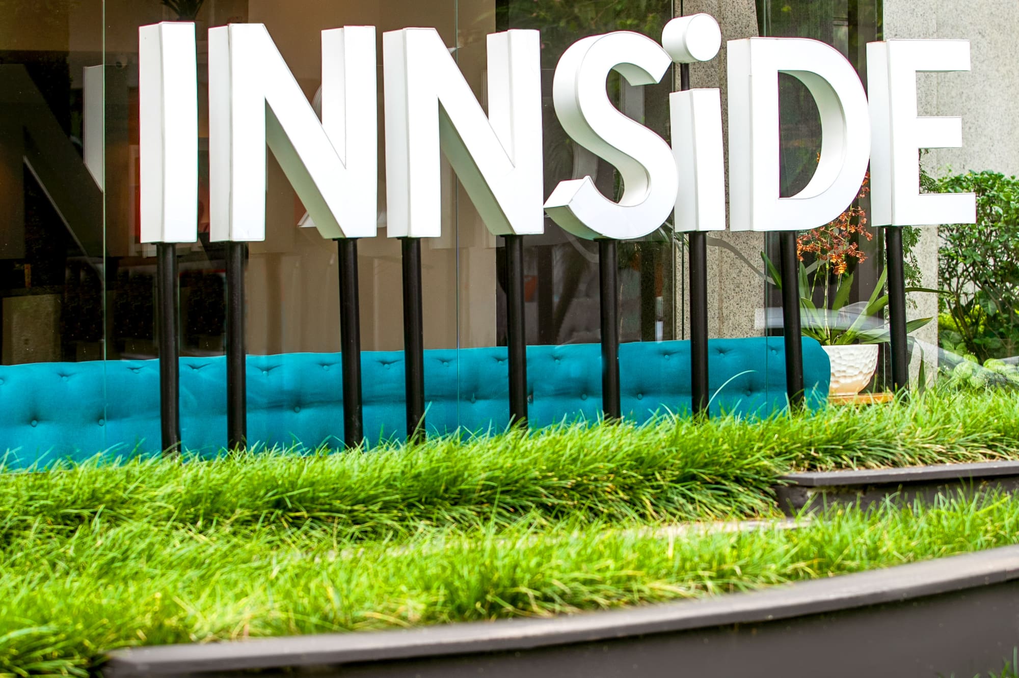 INNSiDE hotel sign outside glass building with green planters and blue seating.
