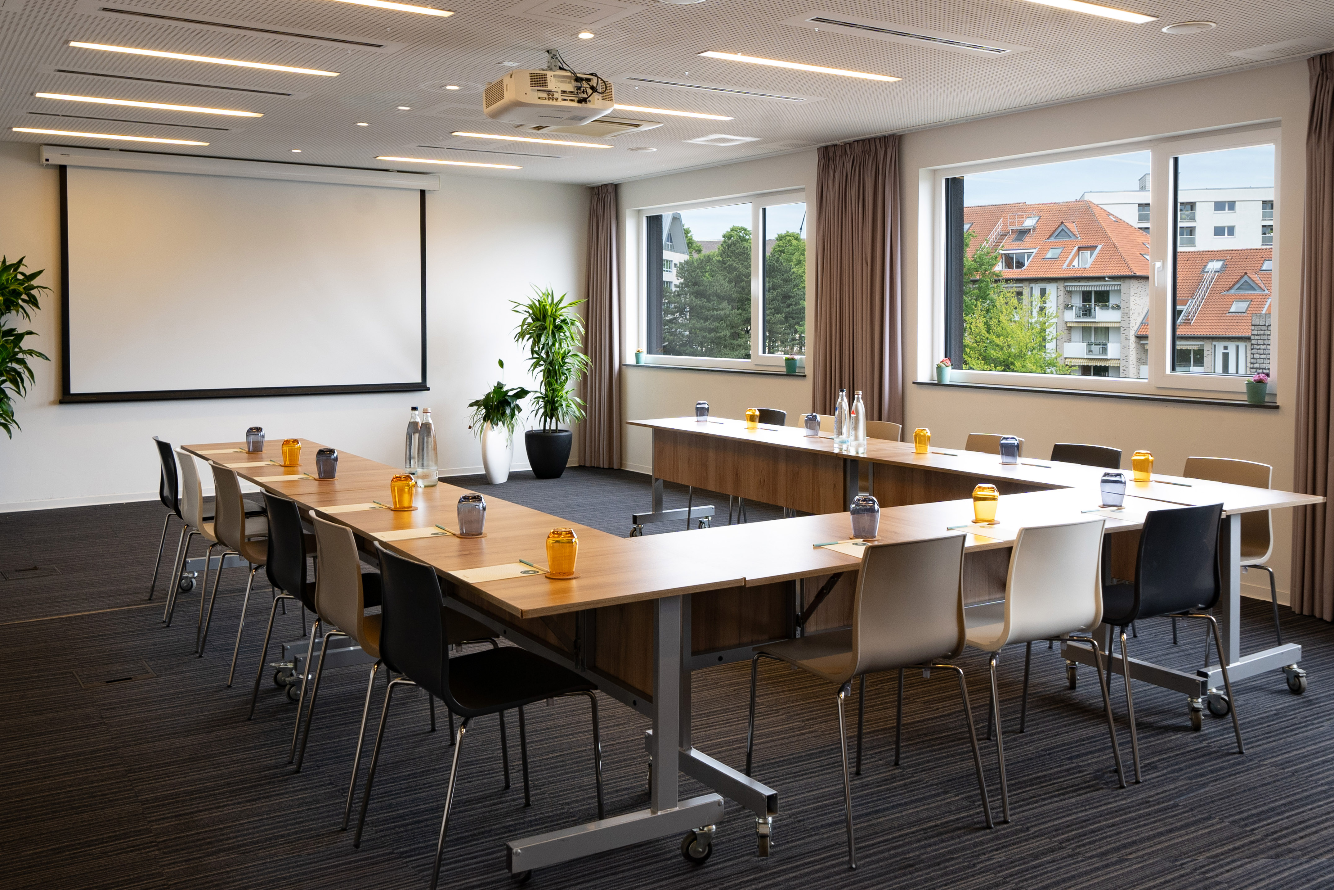 Modern conference room with U-shaped table, projector, screen, and natural light.