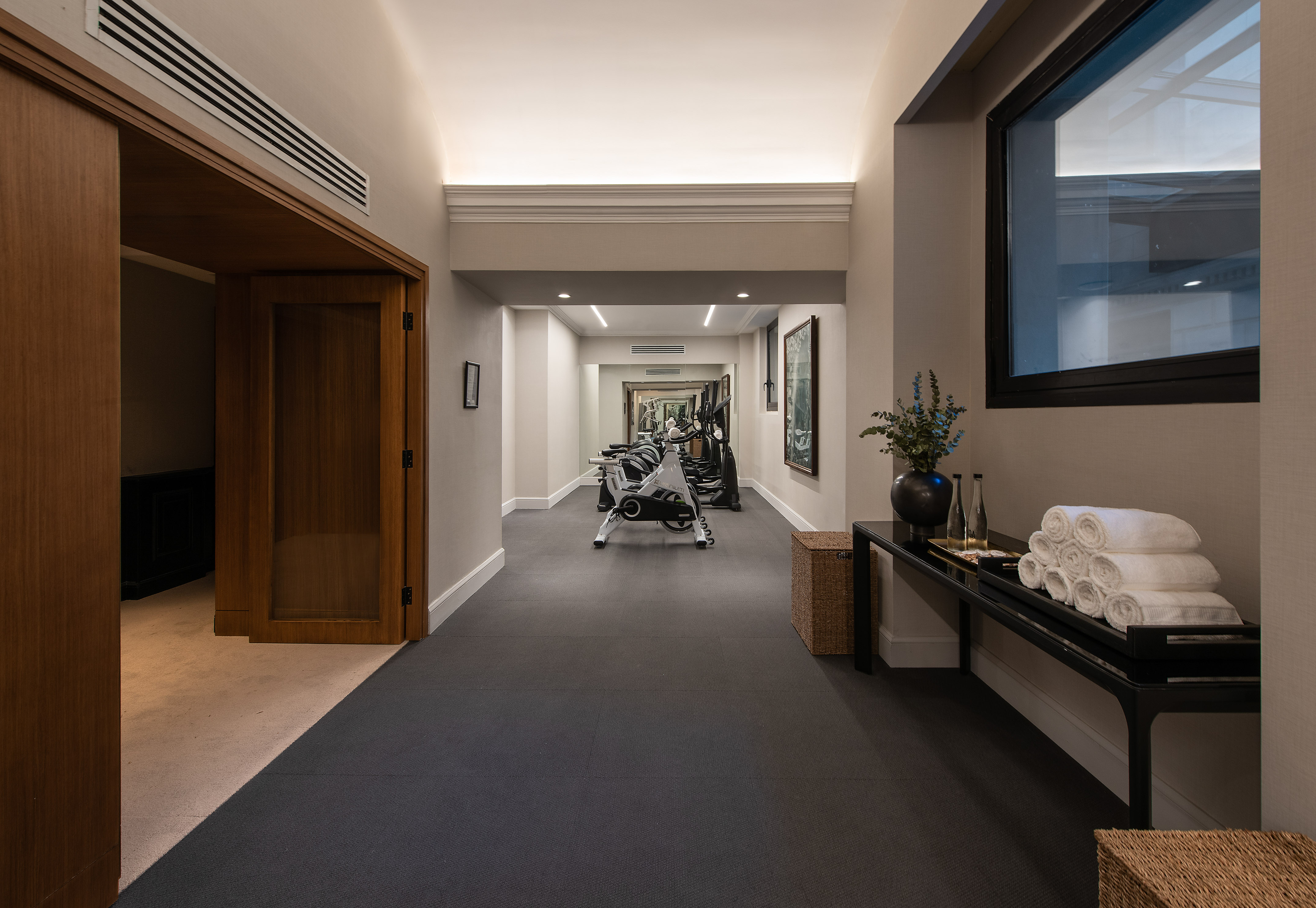 Modern hotel gym hallway with exercise bikes, black flooring, and fresh towels.