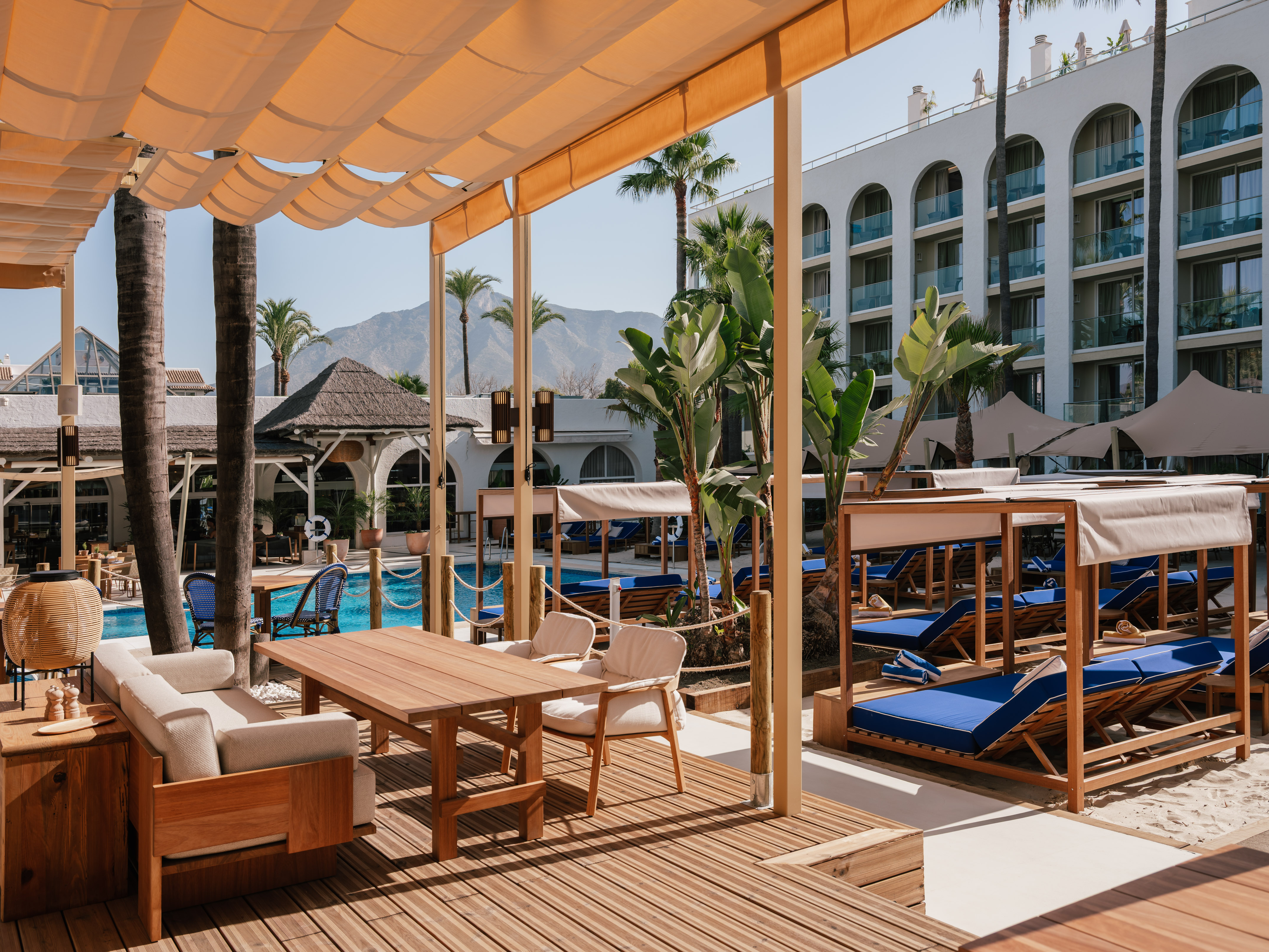 Luxury resort outdoor lounge with pool, palm trees, and mountain views.