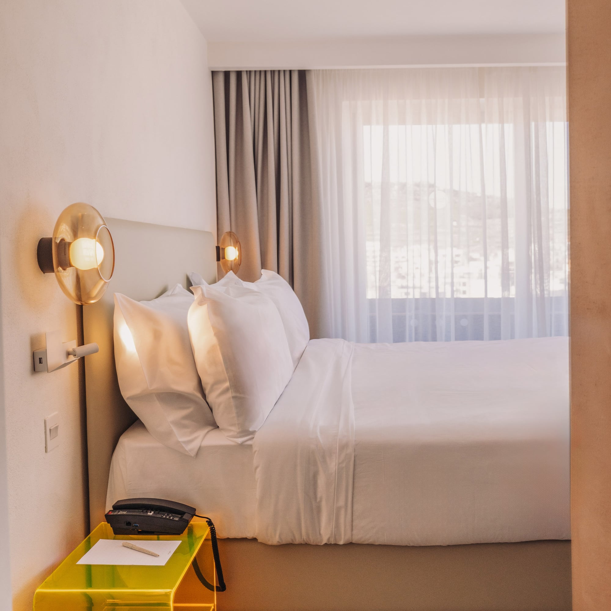 a bed with white sheets and a yellow end table