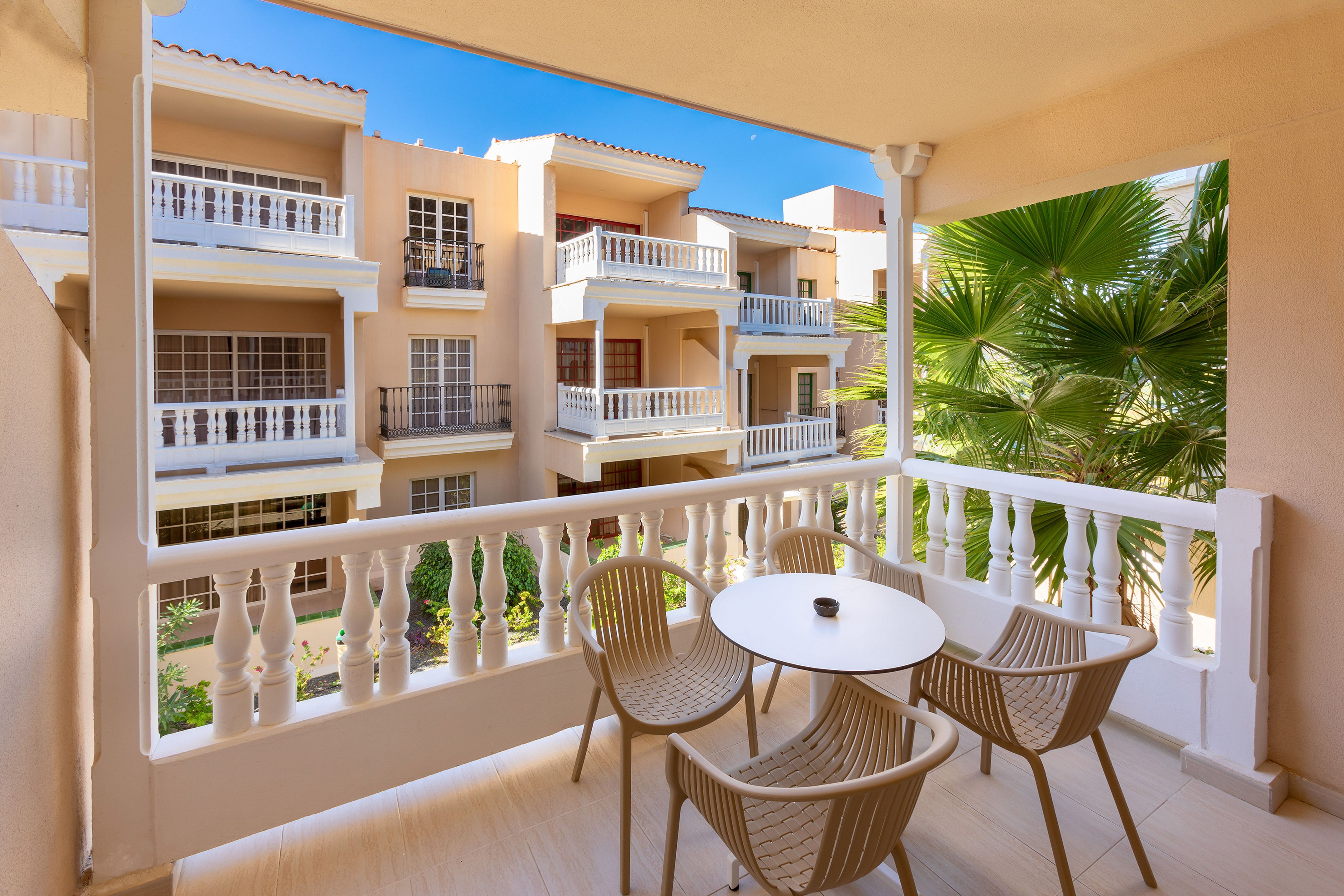 Resort balcony with outdoor table, chairs, white balustrade, apartment view.