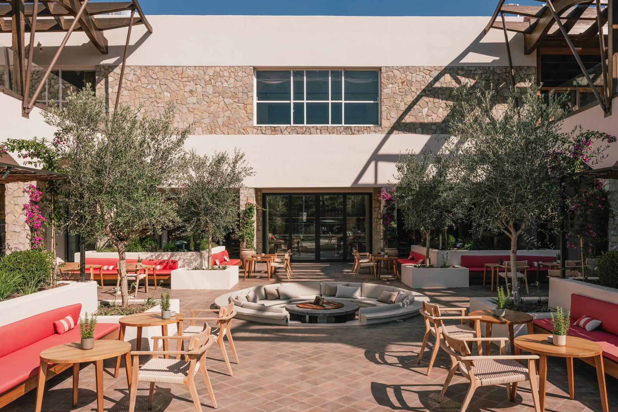 Modern hotel courtyard with outdoor seating, olive trees, and central fire pit.