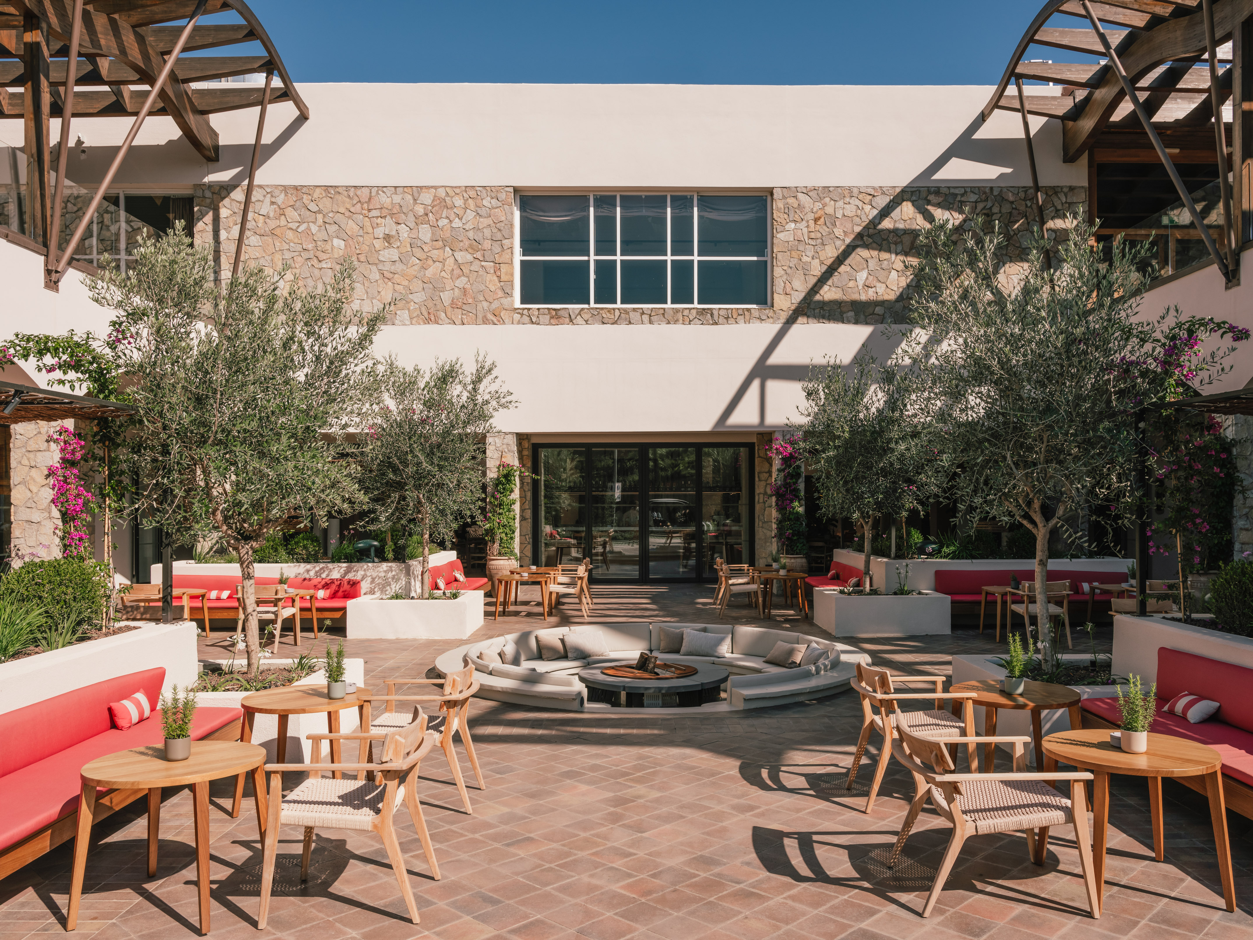 Modern hotel courtyard with outdoor seating, olive trees, and central fire pit.