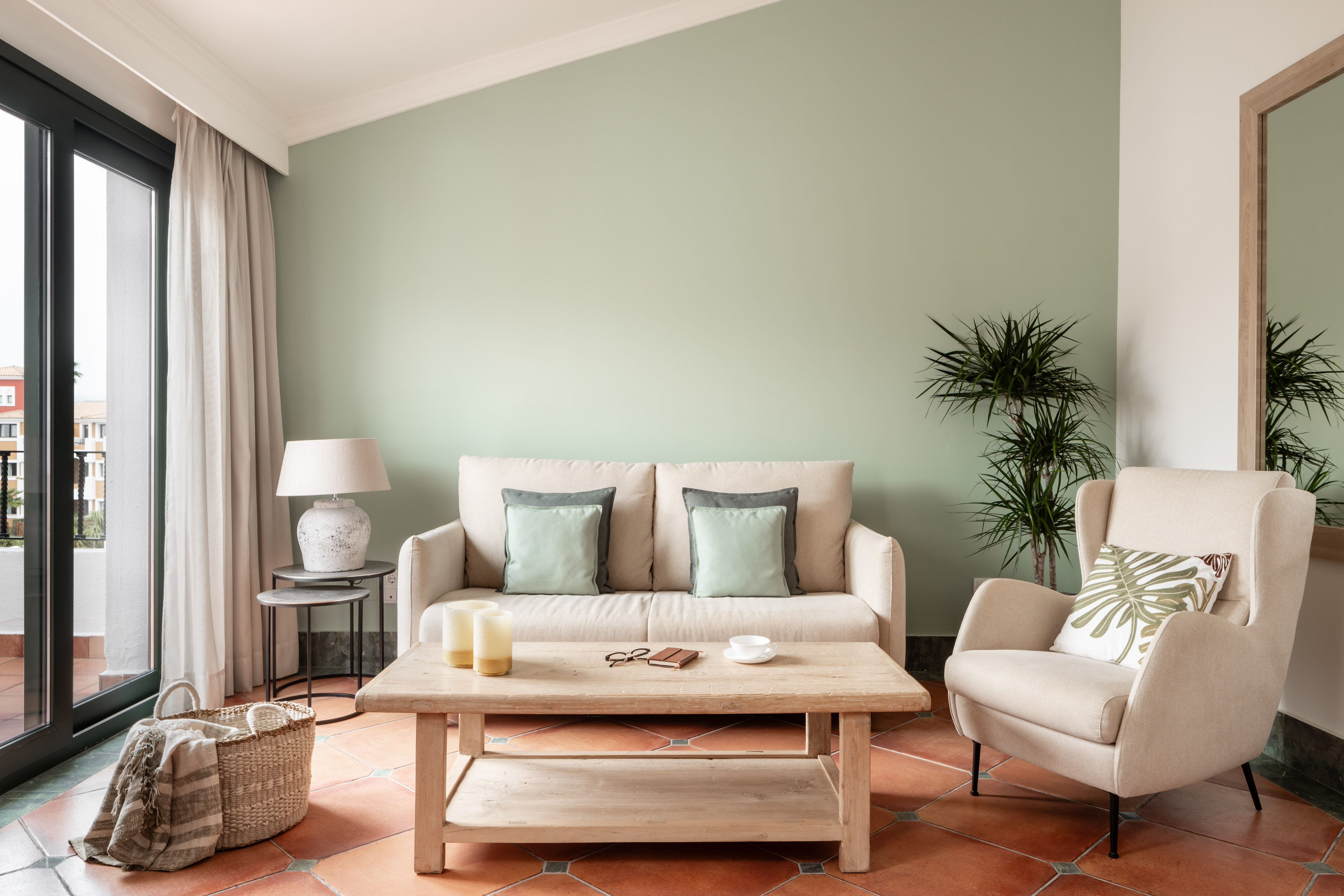 Modern living room with cream sofa, green wall, terracotta floor, and balcony.