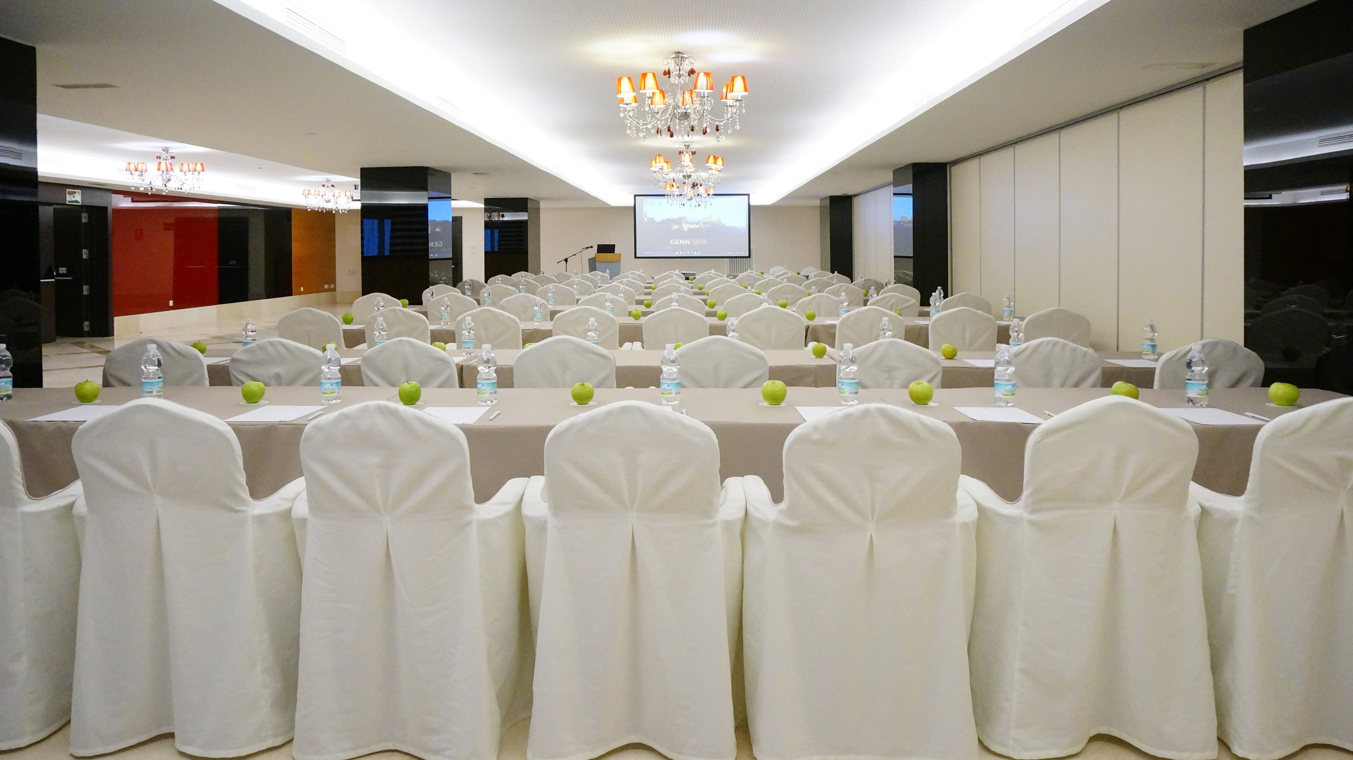 Modern conference room with white chairs, projector, water bottles, green apples.