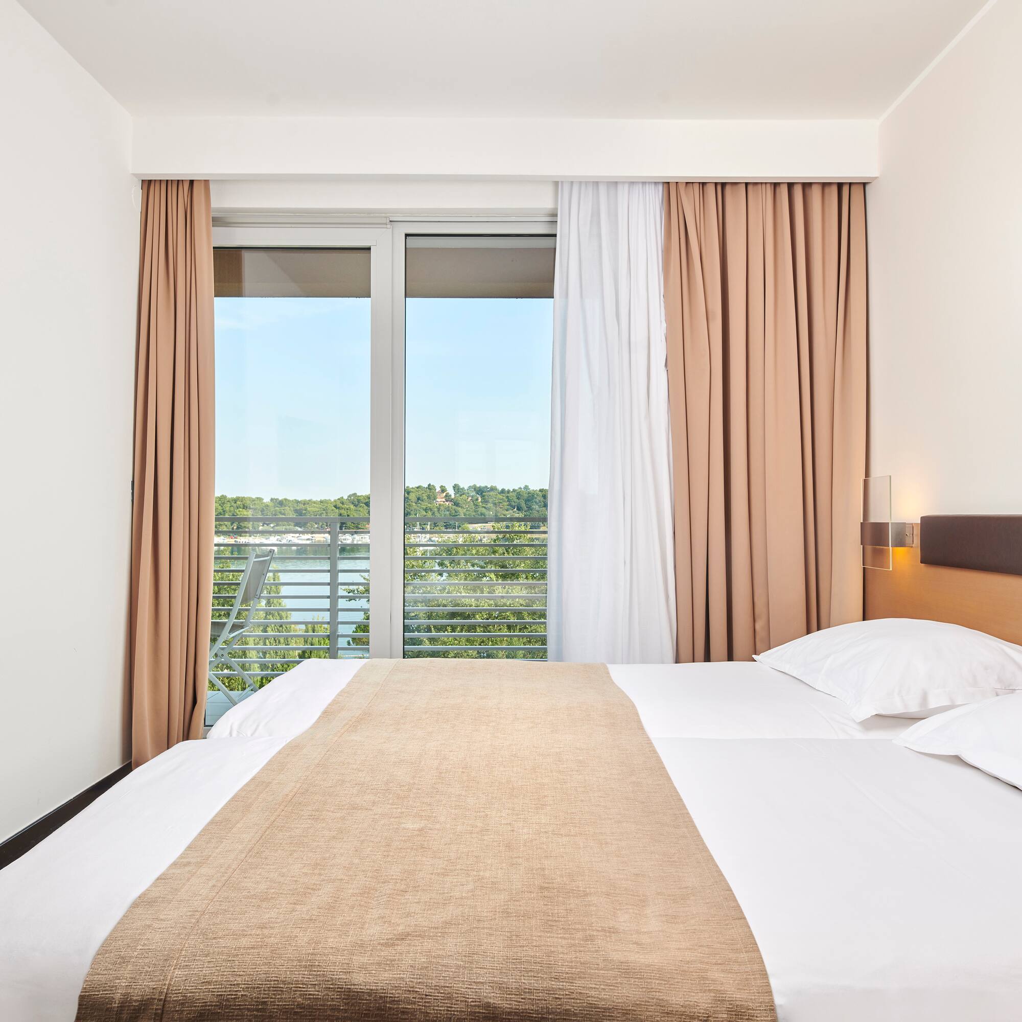 a bed with white sheets and brown blanket in a room with a window