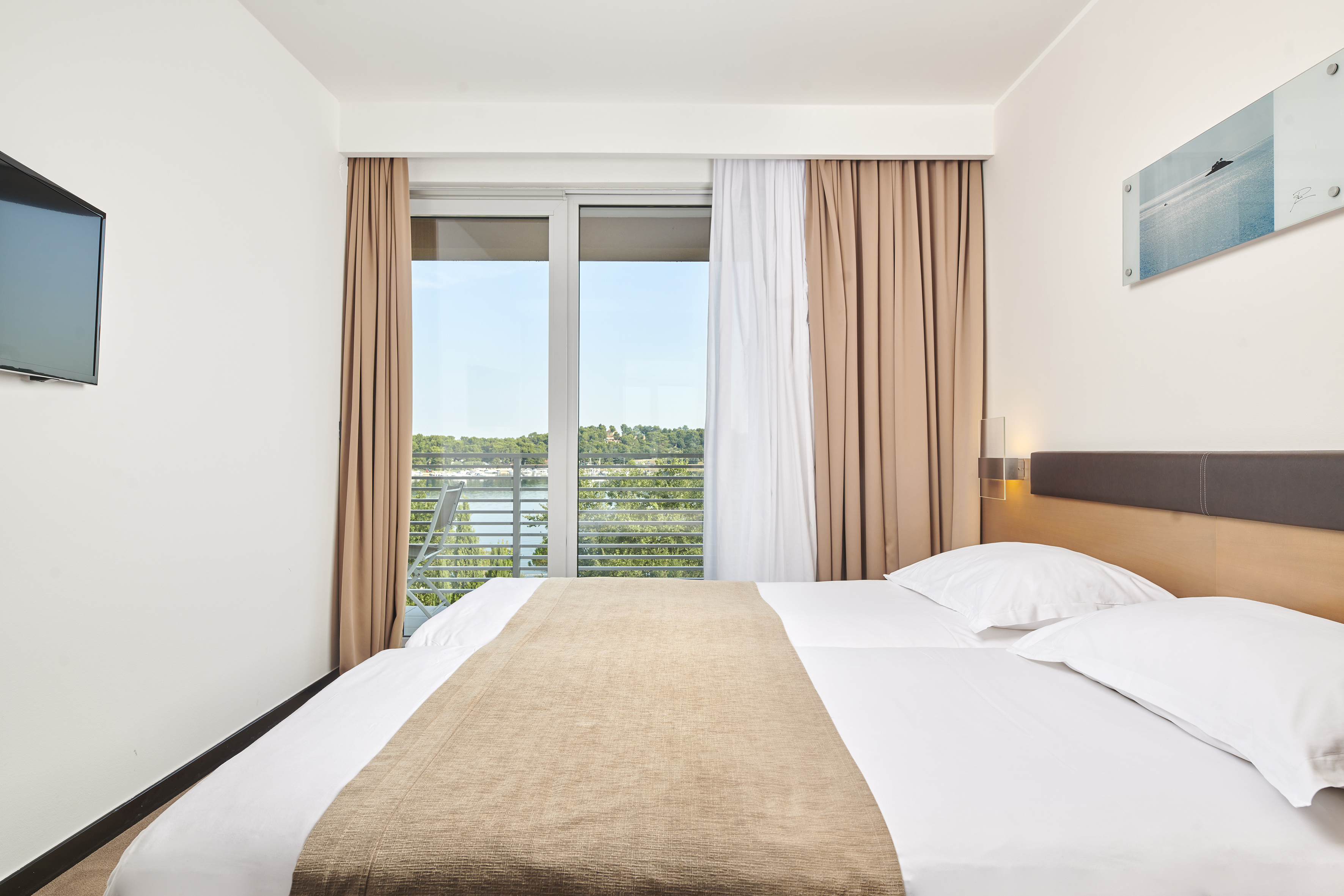 a bed with white sheets and brown blanket in a room with a window