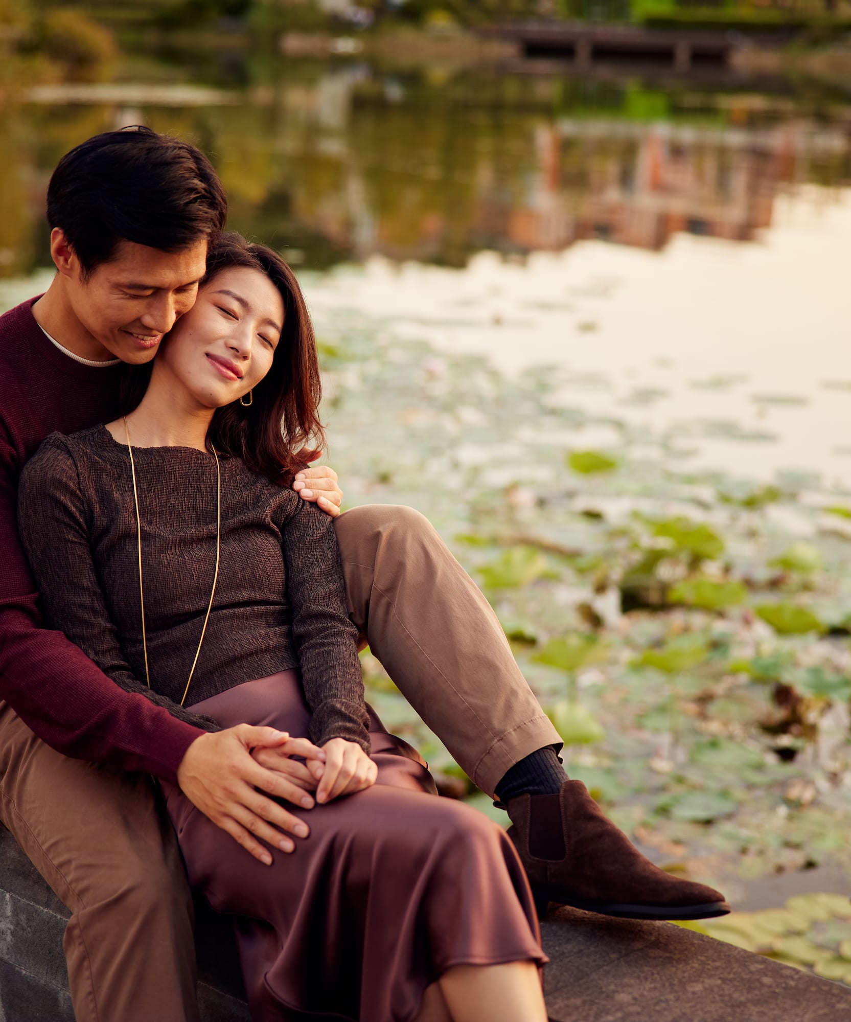 Romantic Asian couple embracing by a pond at sunset.