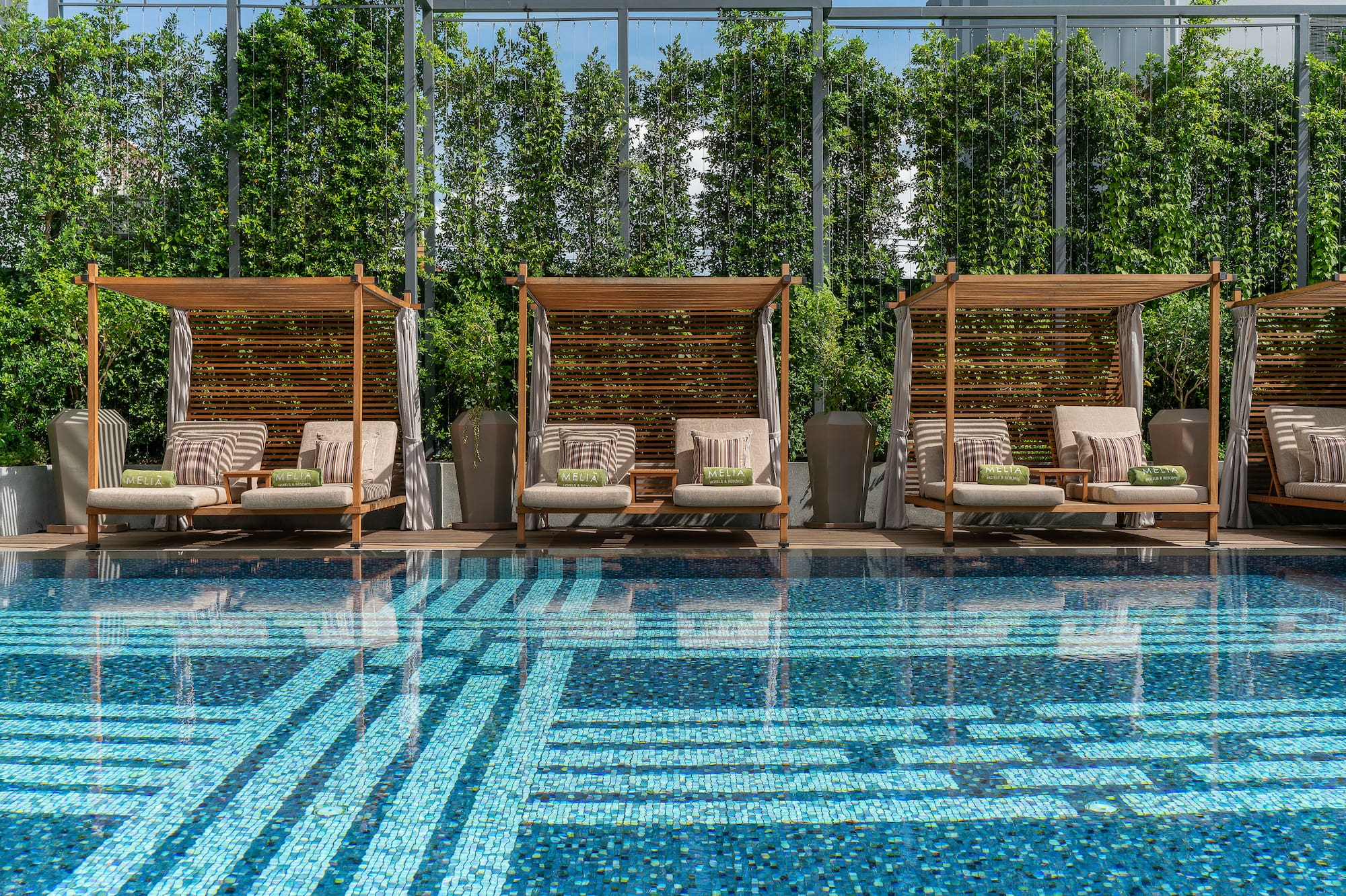 Melia hotel pool: wooden cabanas, blue mosaic swimming pool, lush green hedges.