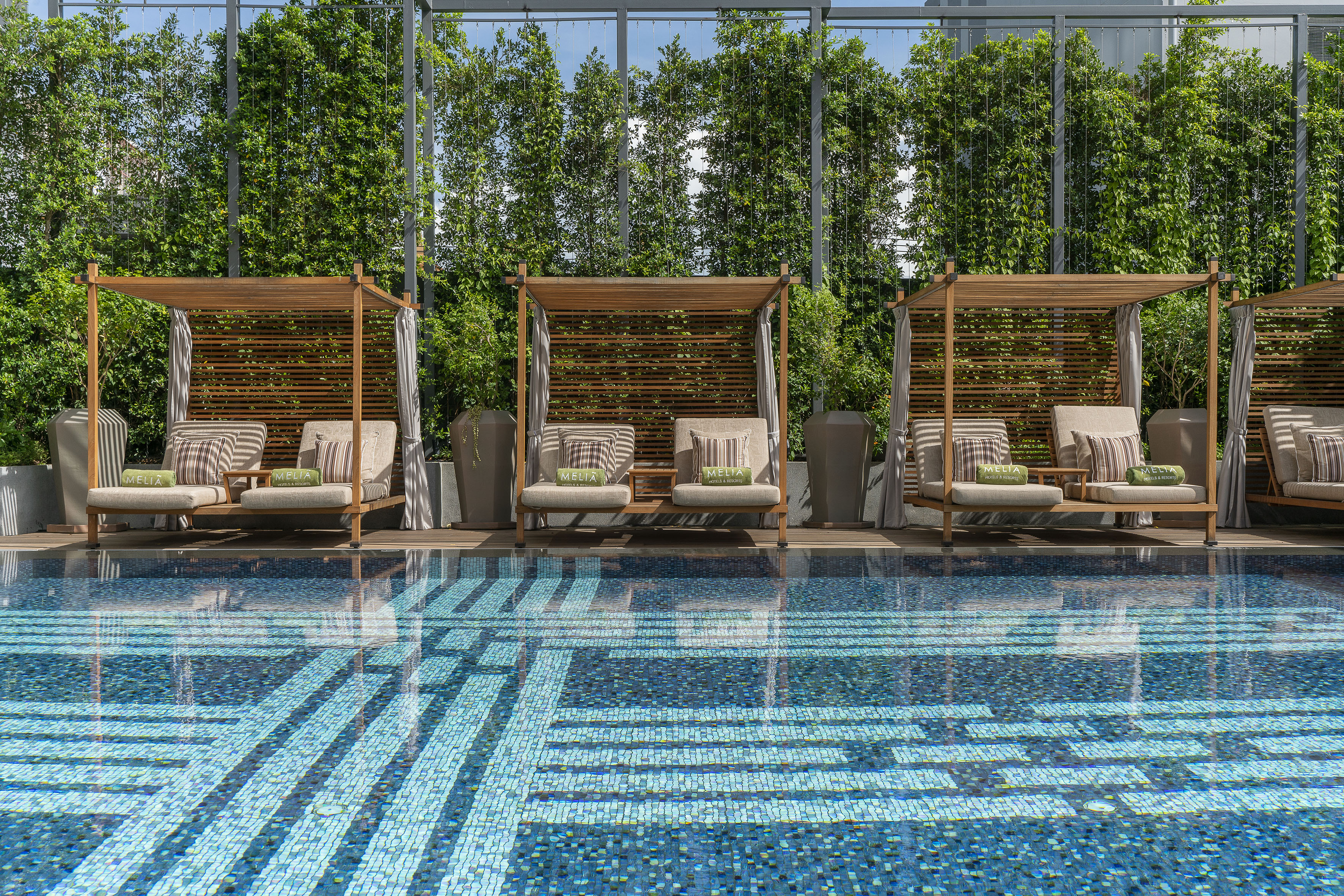 Melia hotel pool: wooden cabanas, blue mosaic swimming pool, lush green hedges.