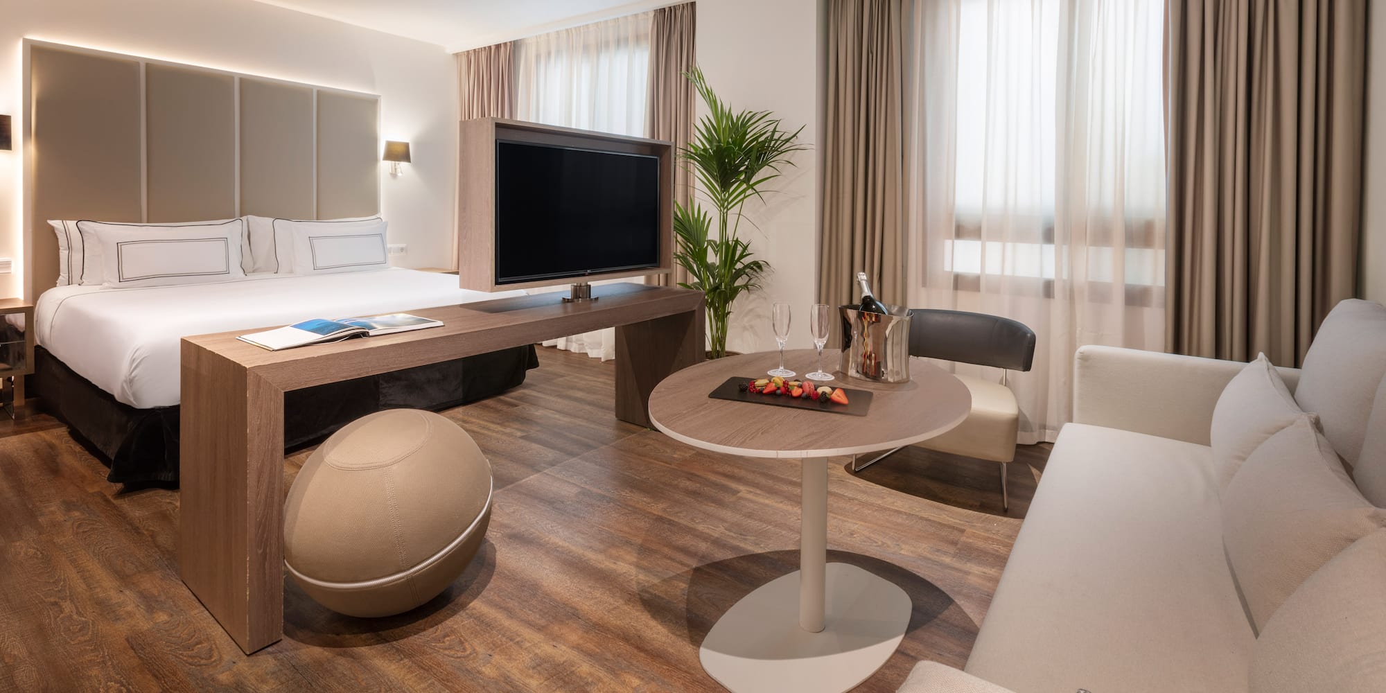 Luxury hotel suite with king bed, TV, lounge area, and welcome champagne.
