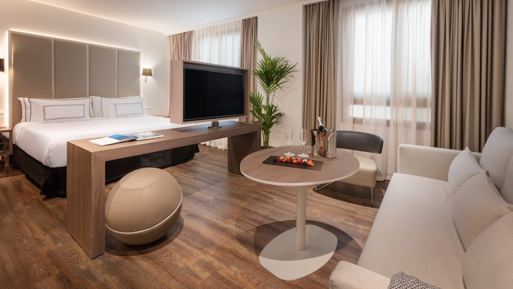 Luxury hotel suite with king bed, TV, lounge area, and welcome champagne.