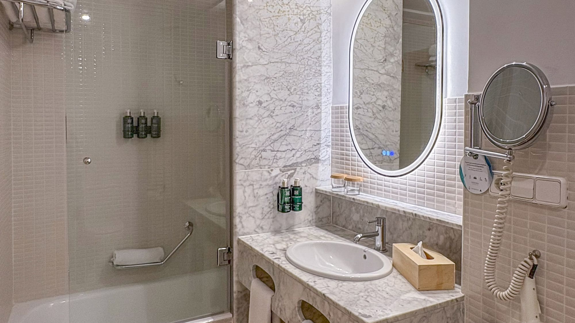 Modern bathroom with marble vanity, oval LED mirror, and bathtub shower.