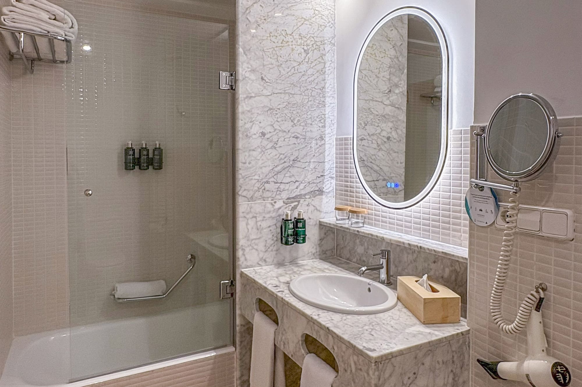 Modern bathroom with marble vanity, oval LED mirror, and bathtub shower.