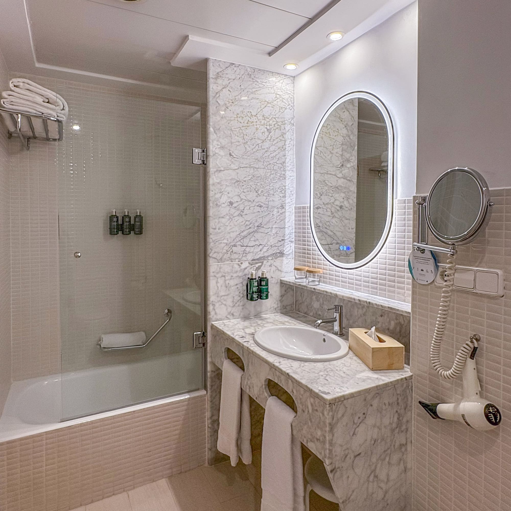 Modern bathroom with marble vanity, oval LED mirror, and bathtub shower.