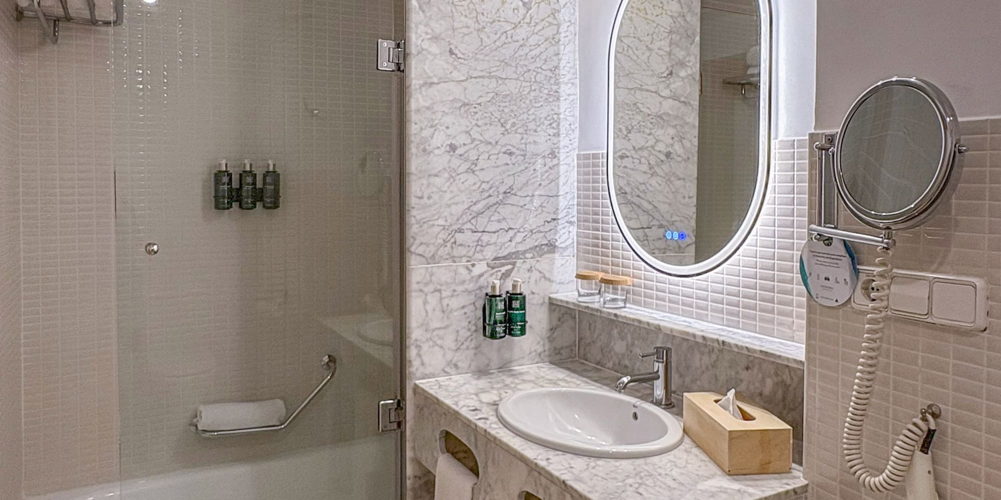 Modern bathroom with marble vanity, oval LED mirror, and bathtub shower.