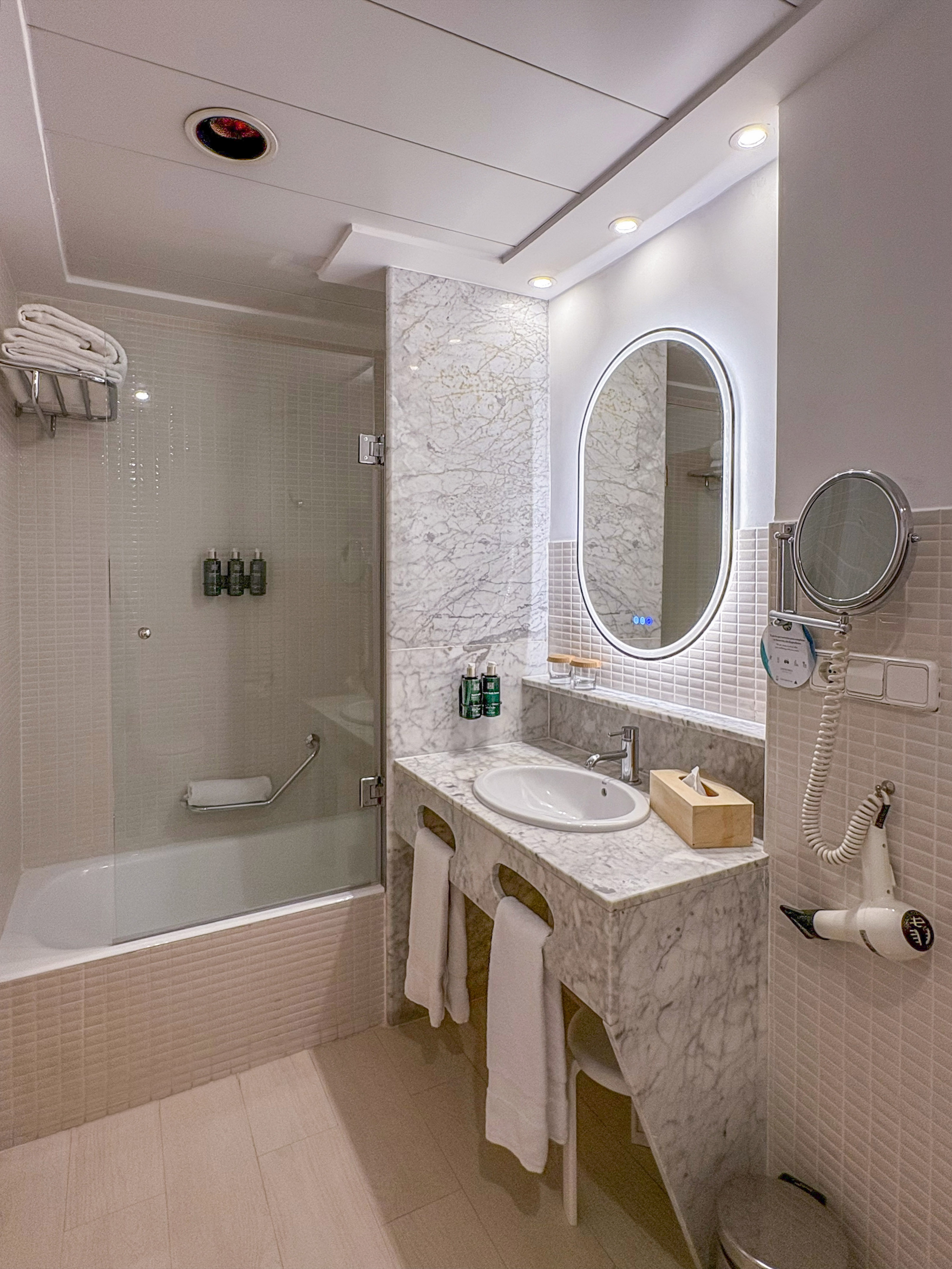 Modern bathroom with marble vanity, oval LED mirror, and bathtub shower.