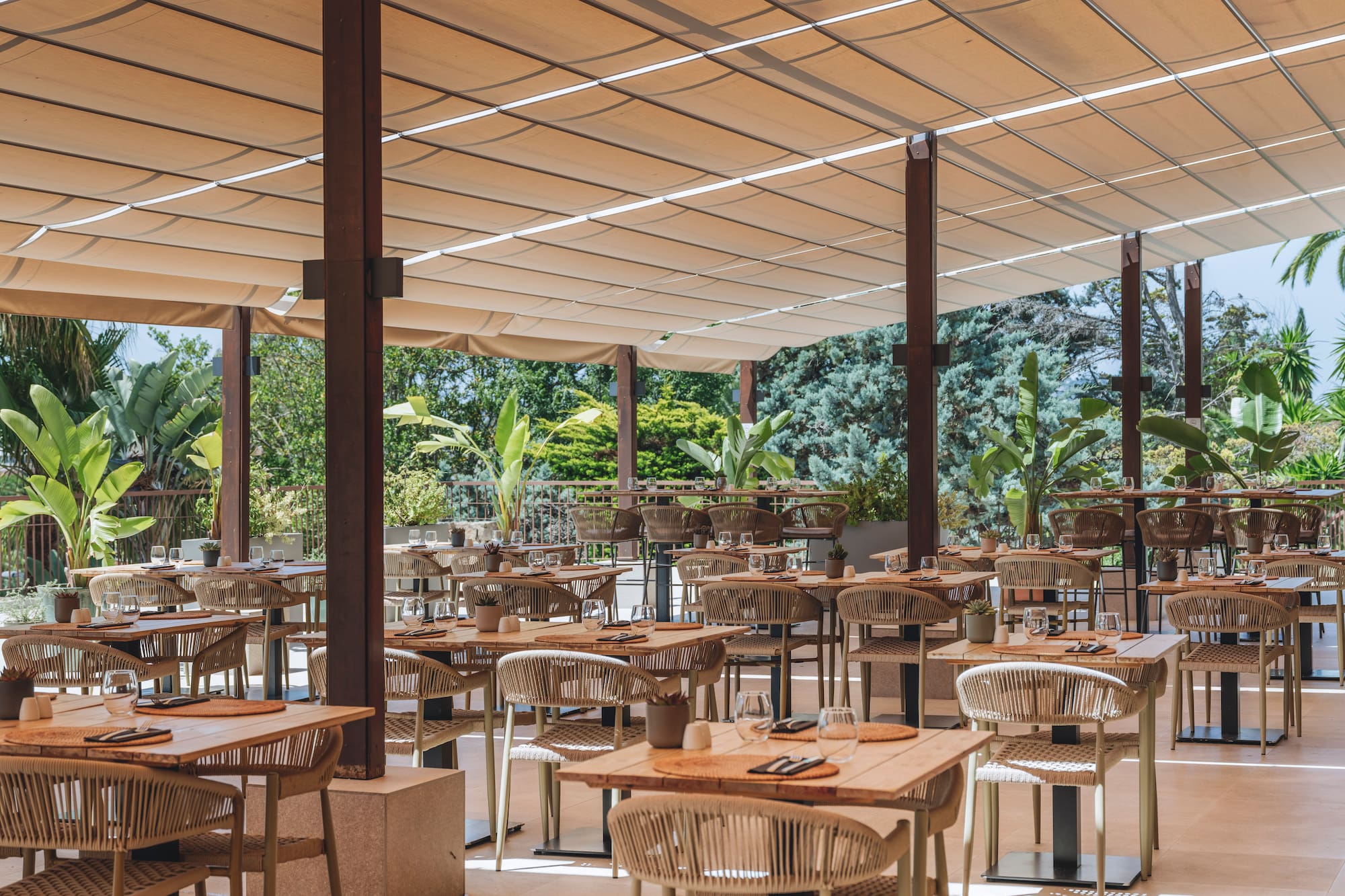 Shaded outdoor restaurant dining area with modern tables and lush greenery.